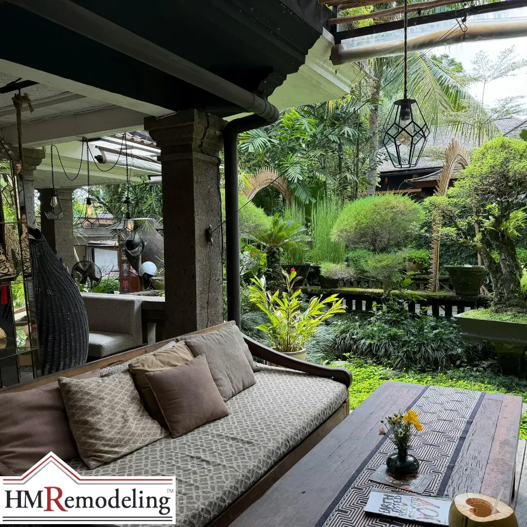 A covered outdoor lounge with a cushioned daybed and pendant light opening onto dense tropical garden foliage, shown as an outdoor living concept for a Michiana area home.