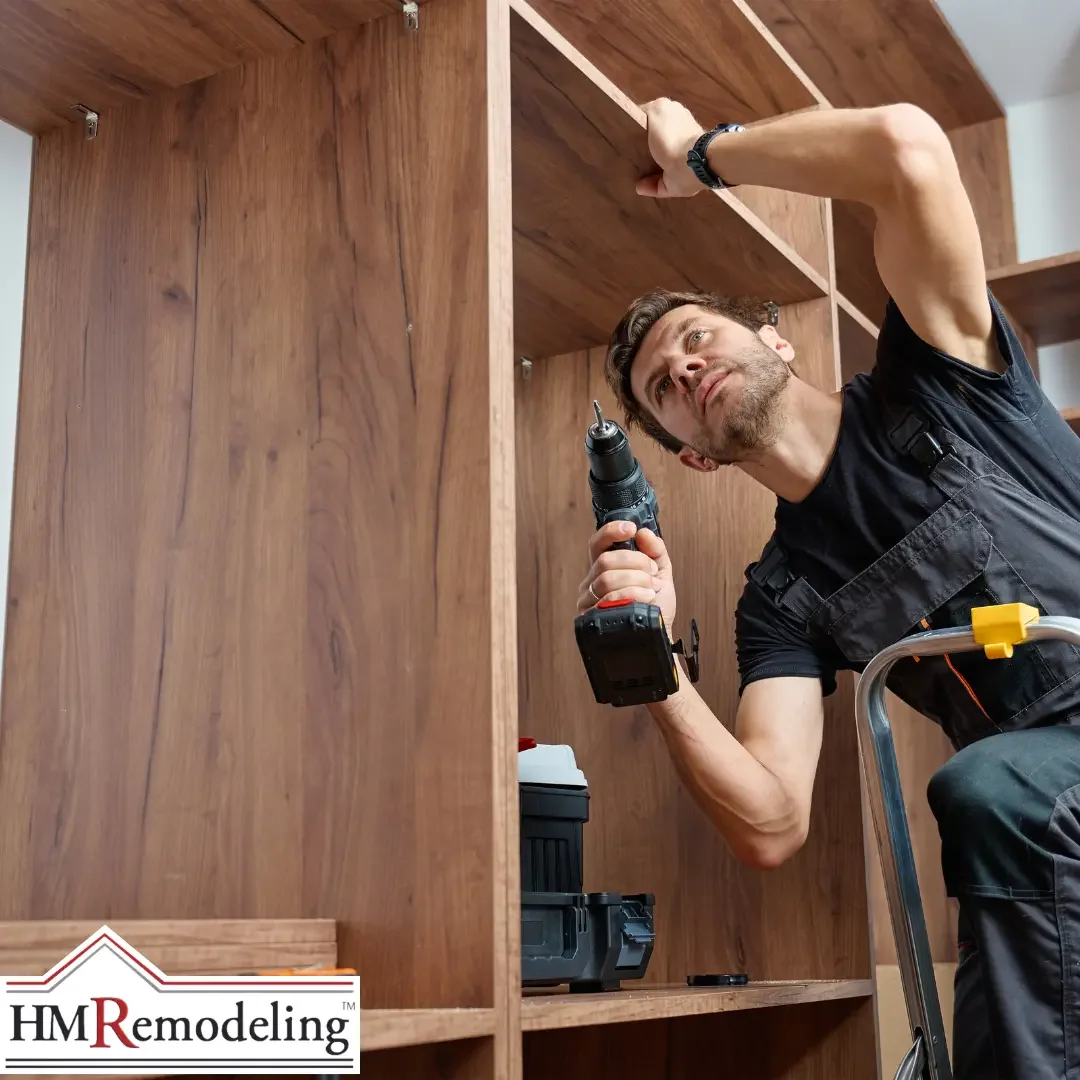 A contractor on a stepladder using a power drill to assemble a large dark walnut wood built-in shelving unit inside a South Bend, Indiana home, with a toolbox resting on a lower shelf
