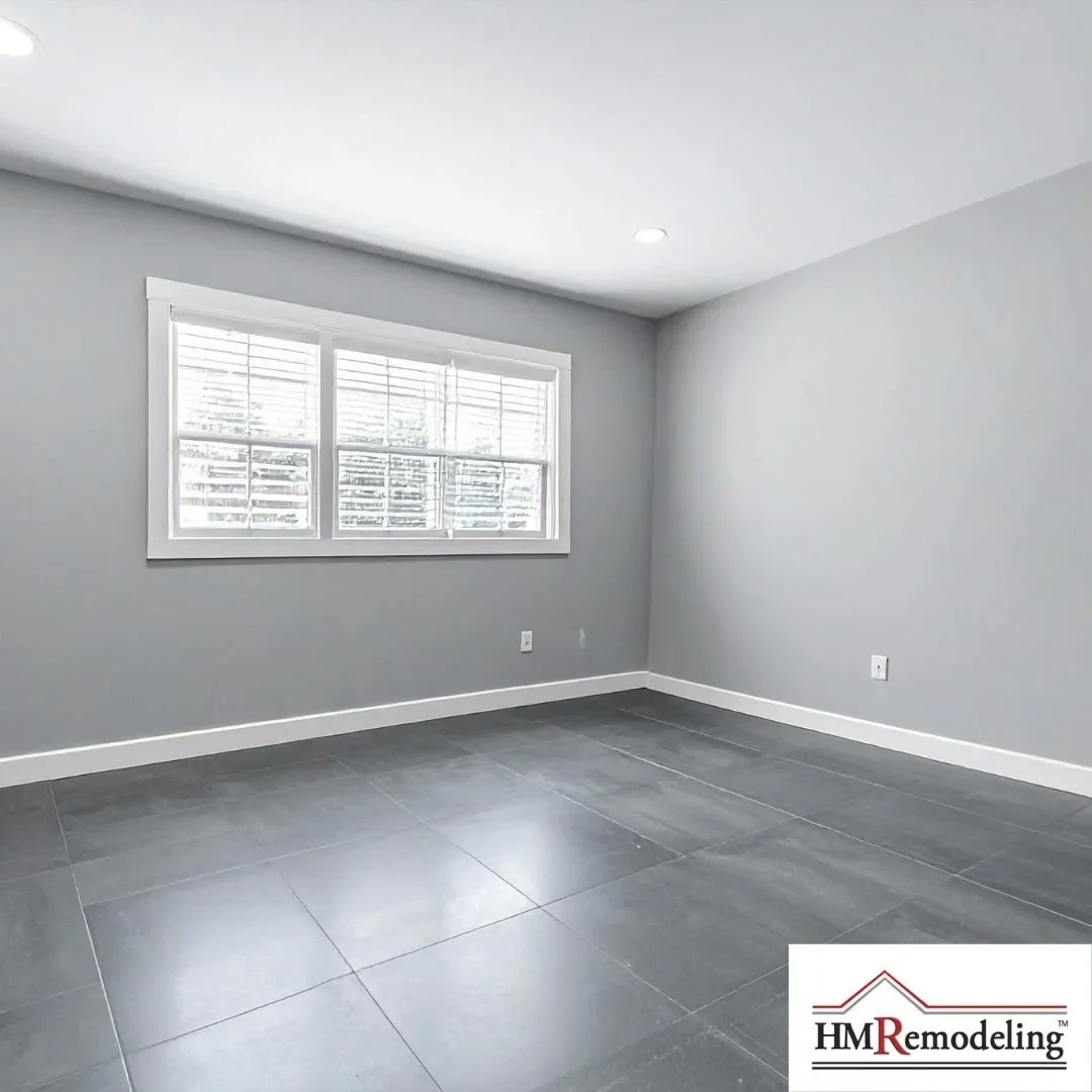Newly remodeled interior room with large gray tile flooring, neutral gray walls, white trim, and a double window with white blinds by HM Remodeling in South Bend, Indiana