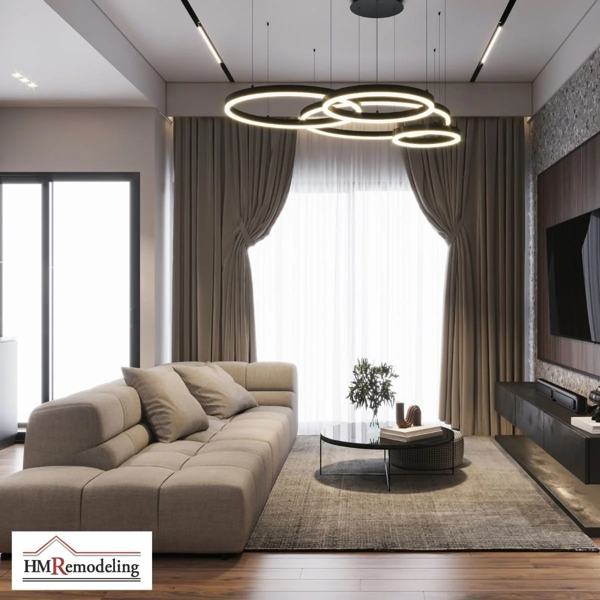 Modern living room remodel with dark hardwood flooring, multi-ring LED chandelier, stone textured accent wall with media console, beige tufted sectional, floor-to-ceiling curtains, and patio door by HM Remodeling in South Bend, Indiana