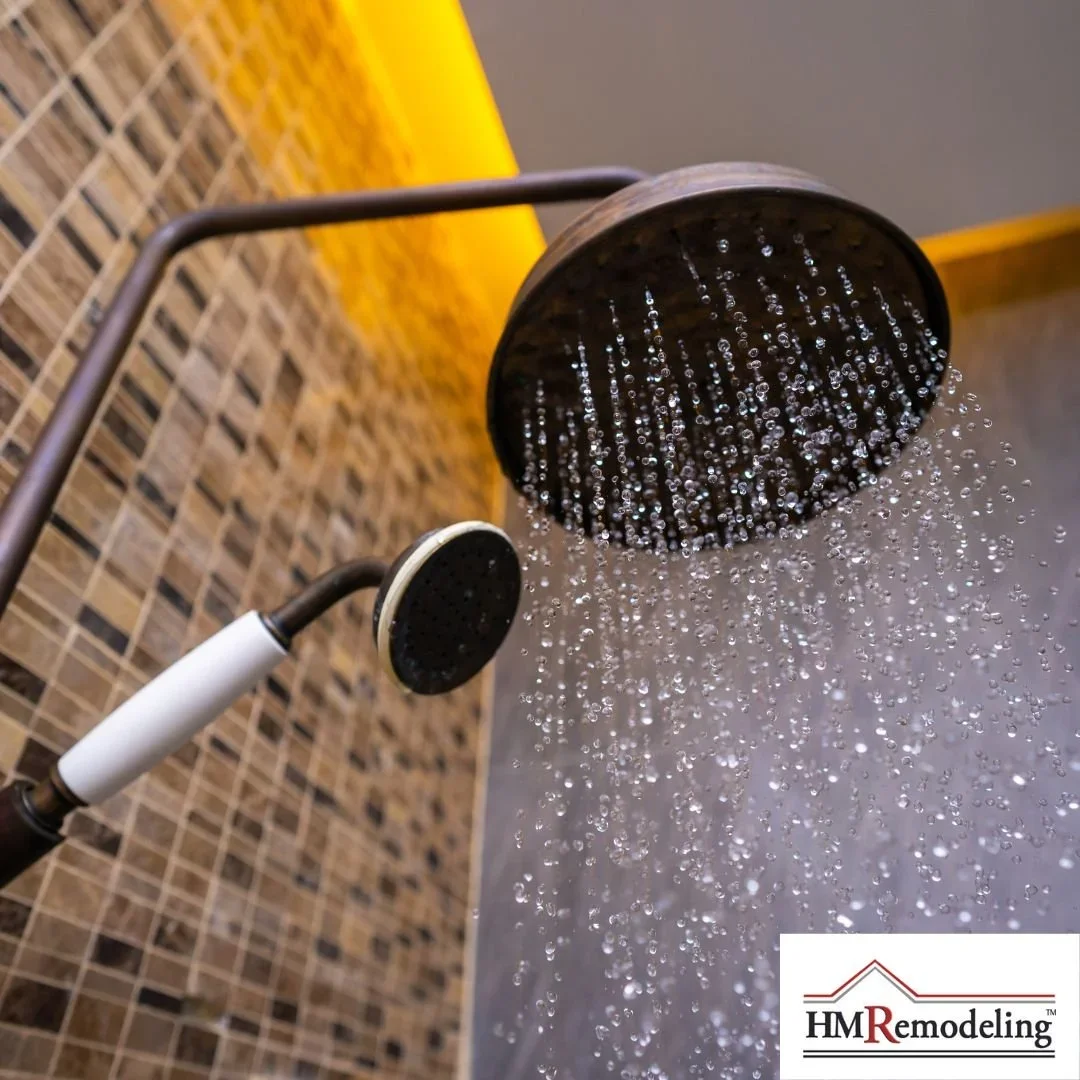 Close-up of oil-rubbed bronze rainfall showerhead and handheld wand running water against mosaic tile shower wall by HM Remodeling in South Bend, Indiana