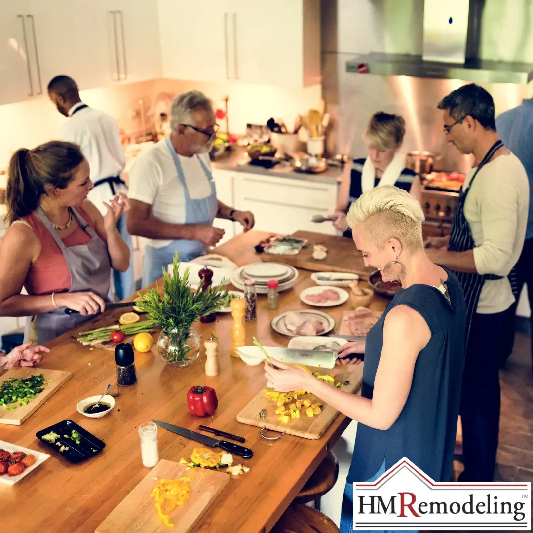 A group of adults cooking and socializing around a large wooden kitchen island with cutting boards, fresh vegetables, and stainless steel appliances in a bright, open-layout kitchen remodeled for entertaining in South Bend, Indiana