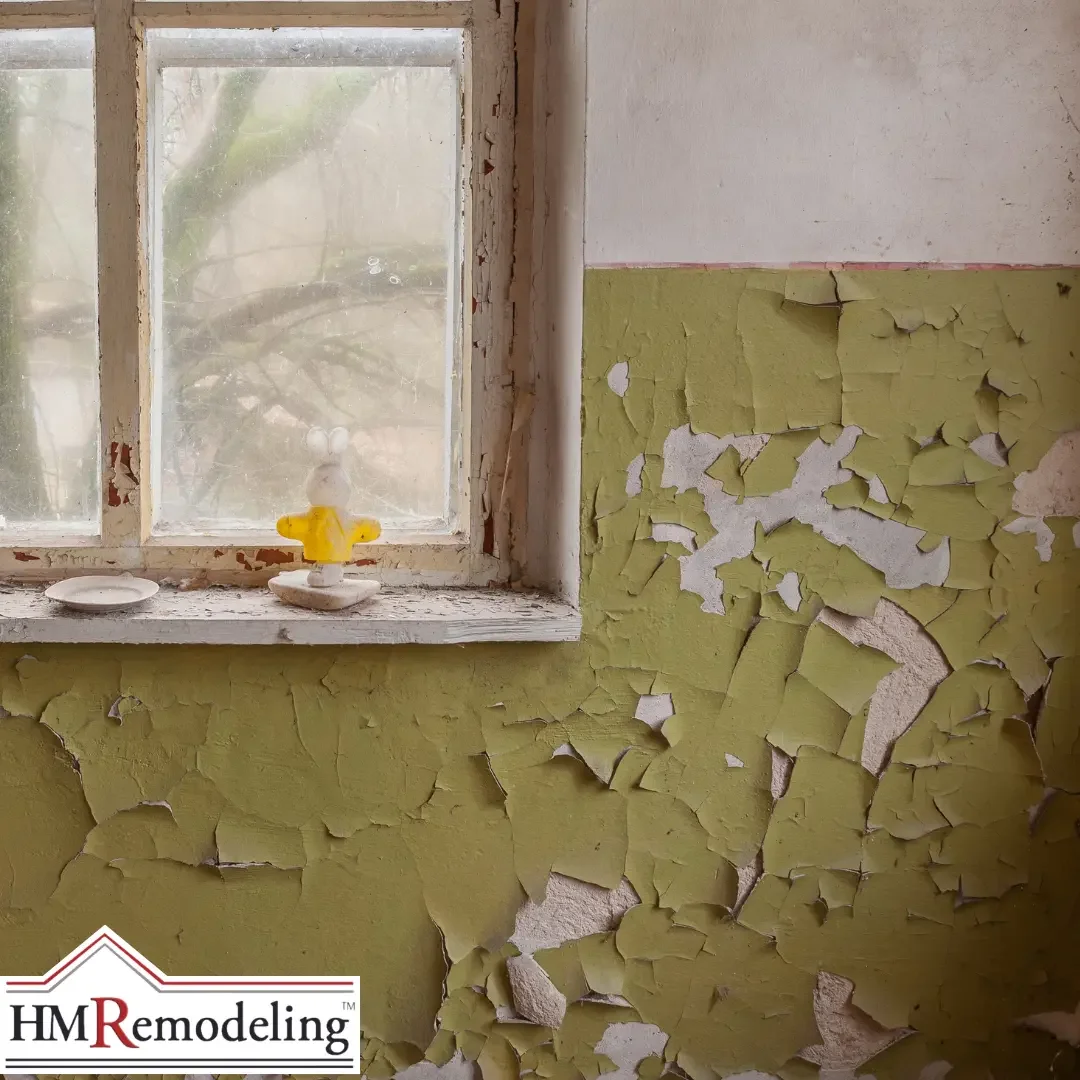A severely deteriorated interior wall in a South Bend, Indiana home with green paint peeling and flaking away from the plaster surface near a wood-framed window, illustrating the effects of lake-effect humidity cycling on interior surfaces
