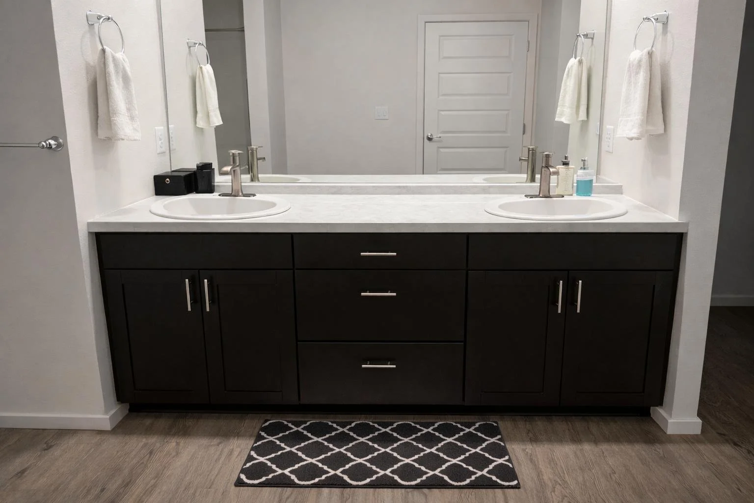 A bathroom vanity with two sinks, dark brown cabinet, white countertop, two mirrors, and towel bars with white towels.