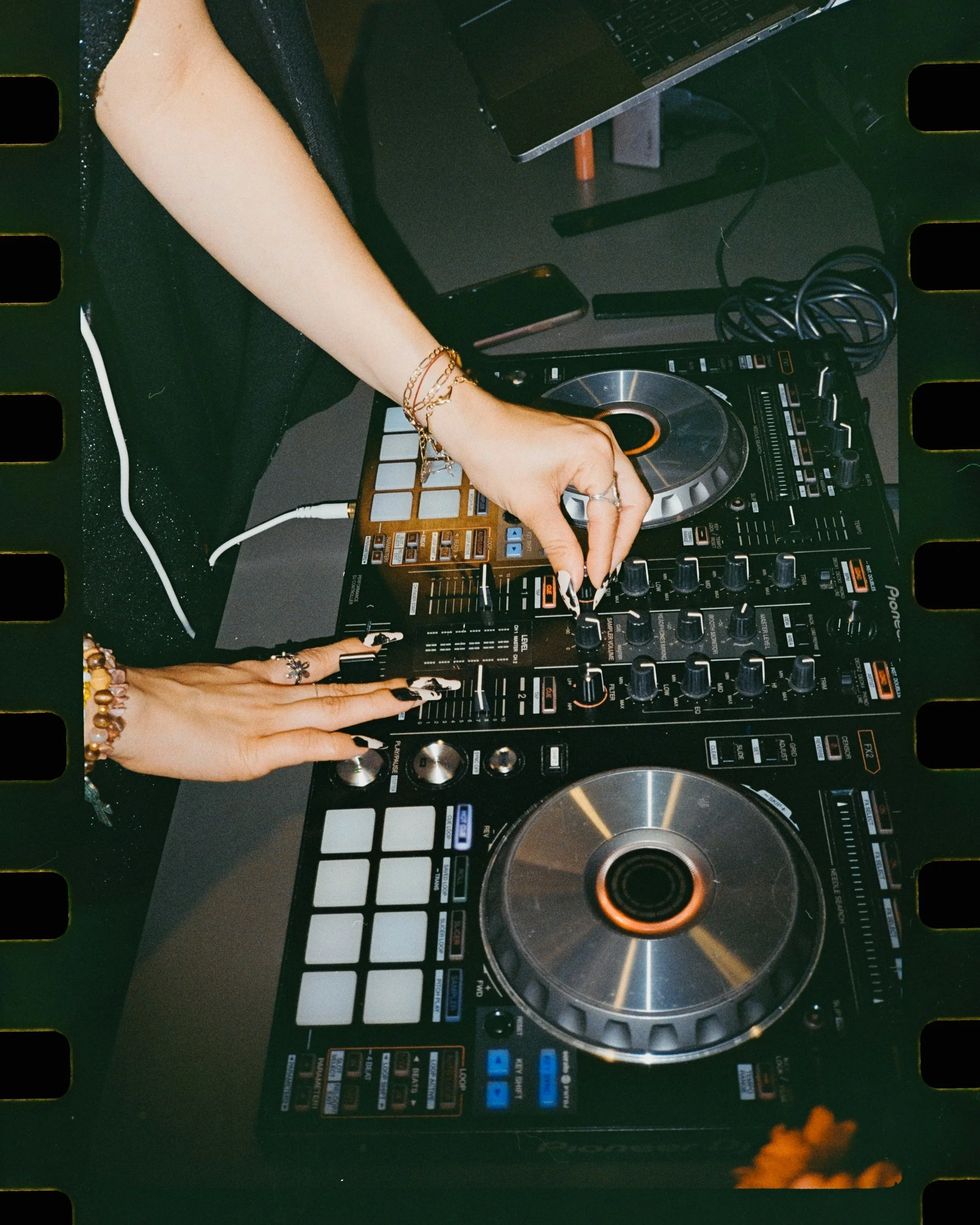 A person using a DJ controller with a laptop and smartphone nearby, likely DJing at an event or personal setting.