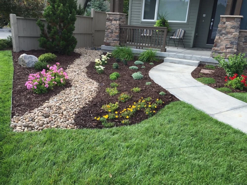 Front yard with well-maintained green lawn, colorful flowers, a curved concrete pathway, and a porch with a bench and potted plants.