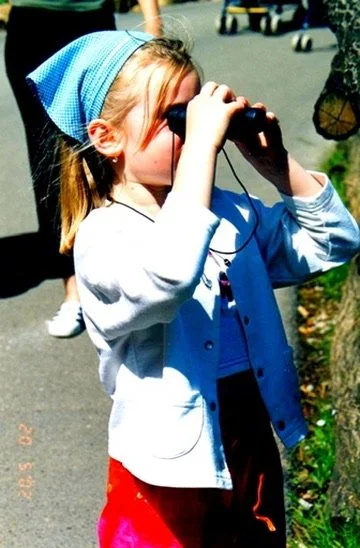 A young girl using binoculars while outdoors.