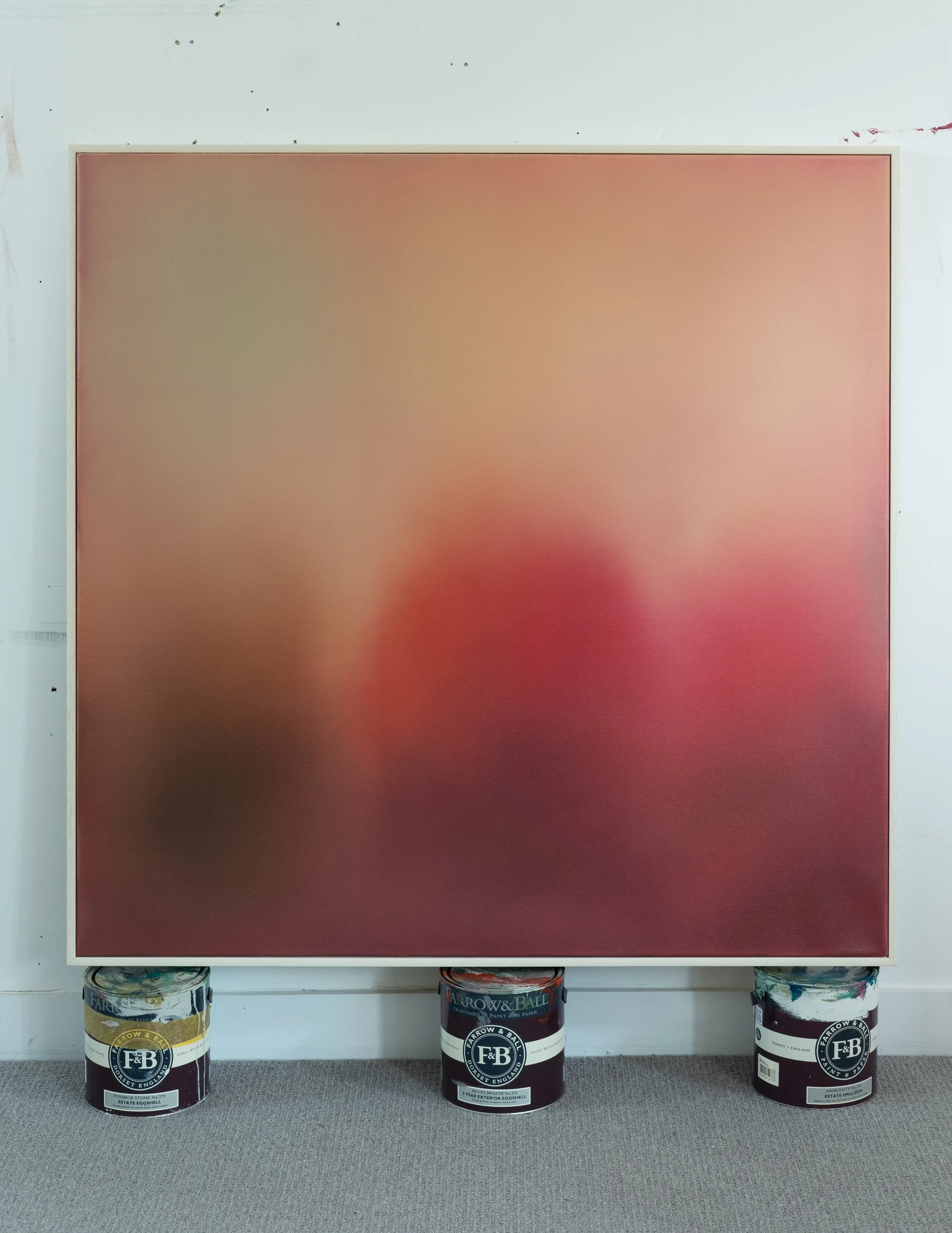 A large painted canvas or panel in progress, mounted on a wall with three paint cans at the base, situated on a gray carpeted floor.