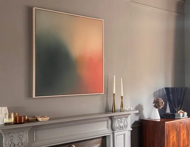 A living room with a decorative gray fireplace mantel, abstract art painting, two tall candlesticks, and various decorative items on the mantel and a wooden sideboard.