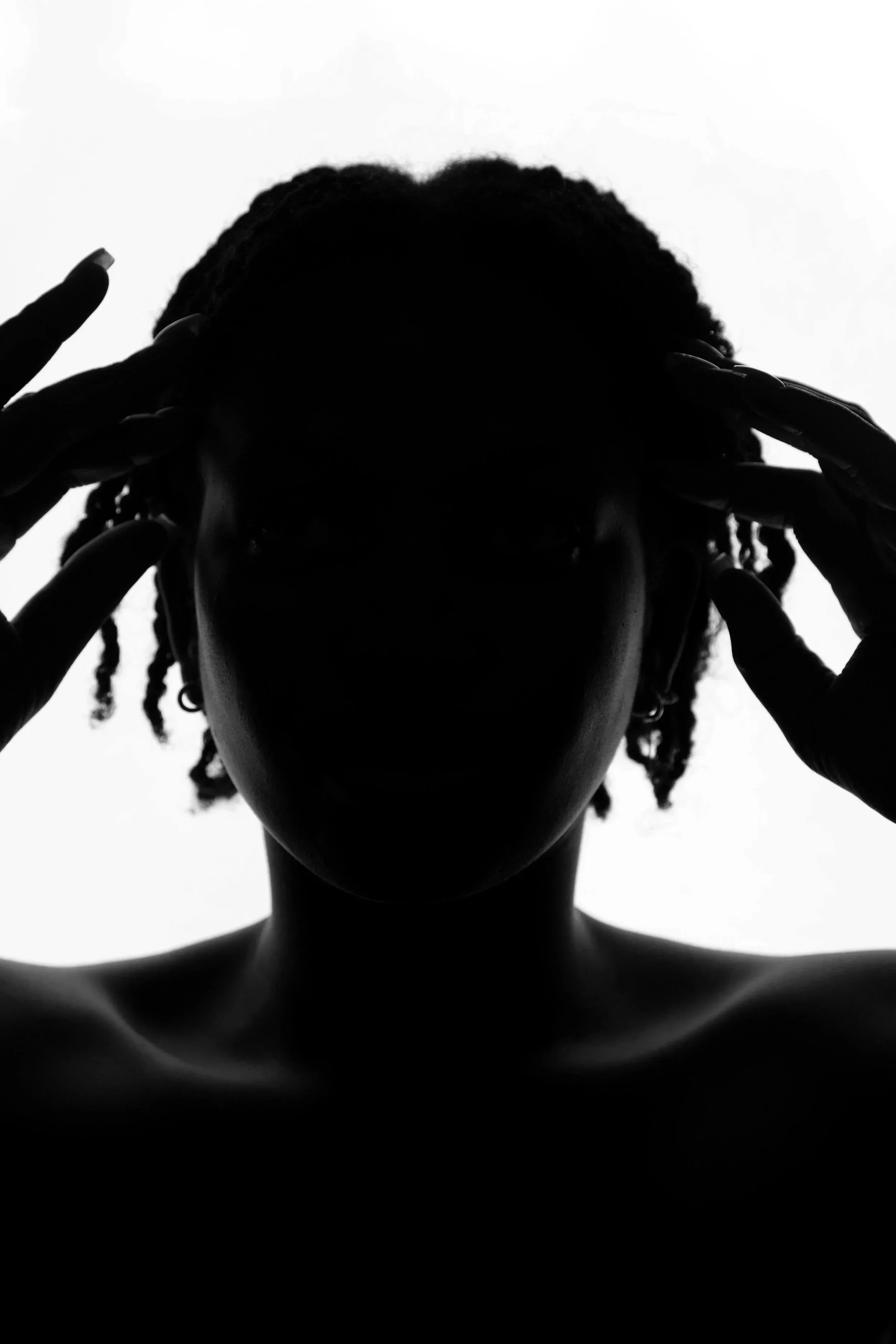 Silhouette of a person with locks holding their head with both hands against a plain light background.