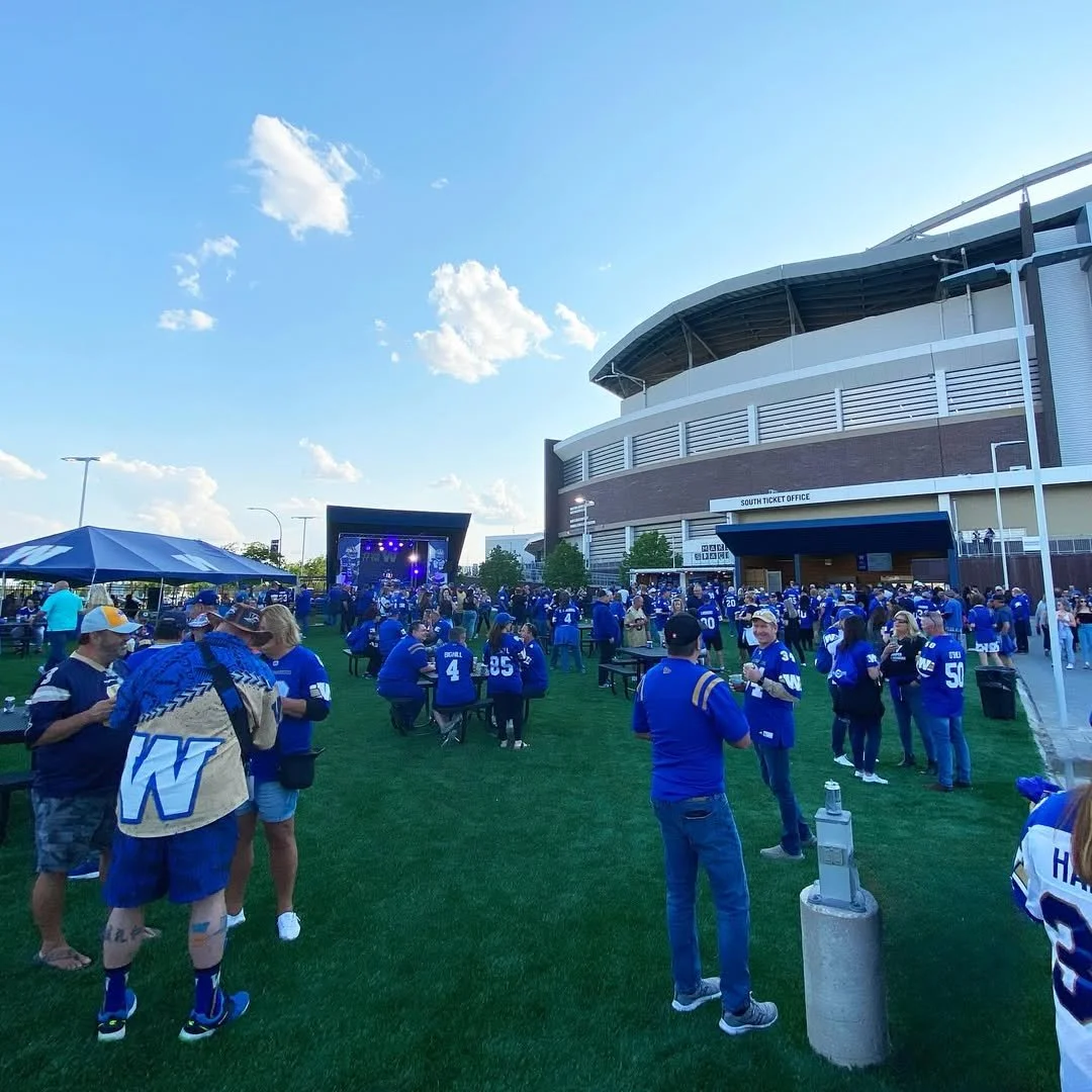 Crowd of people wearing blue jerseys outside a stadium watching a concert on a stage under a clear blue sky.