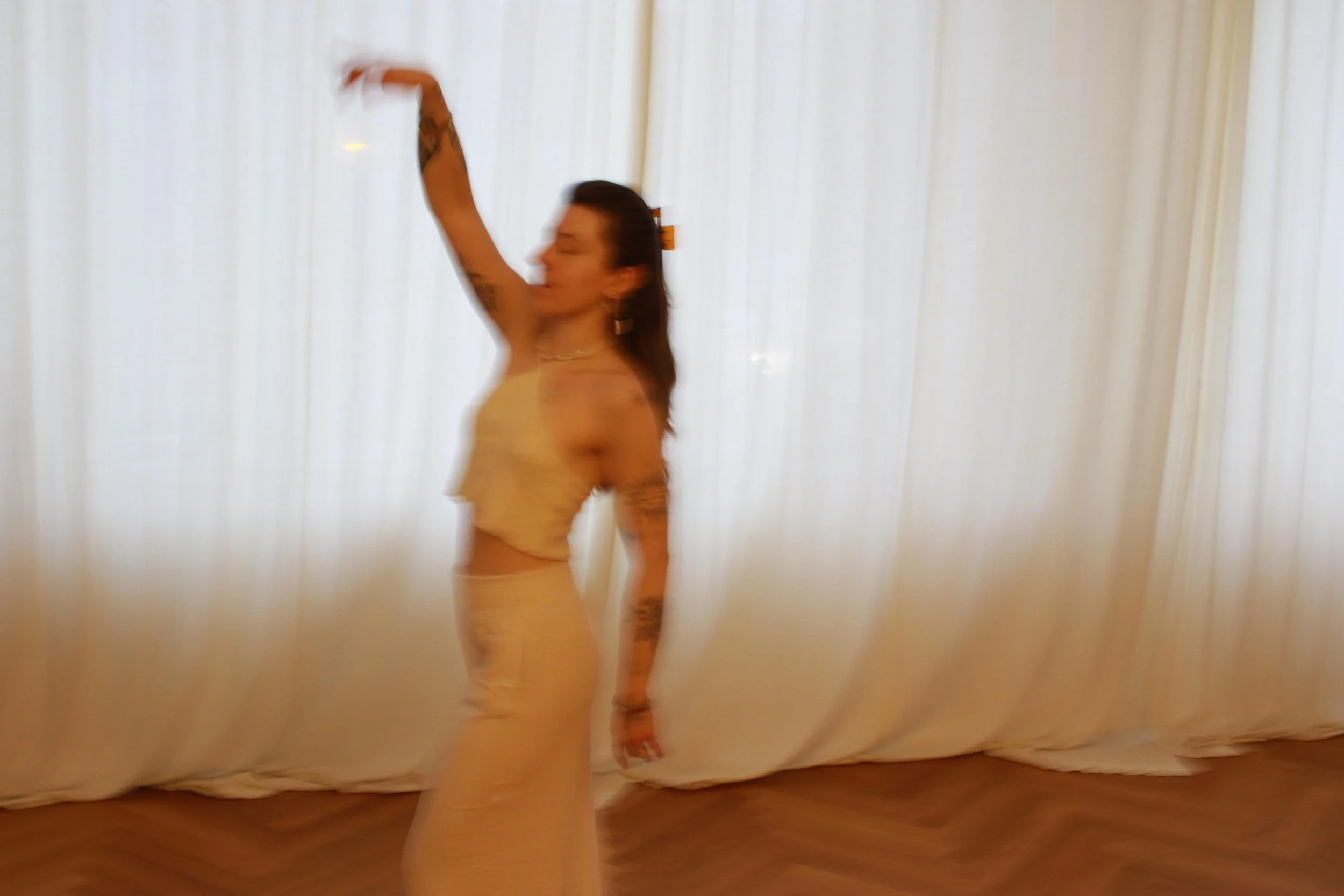 A woman with tattoos dancing in front of a white curtain.