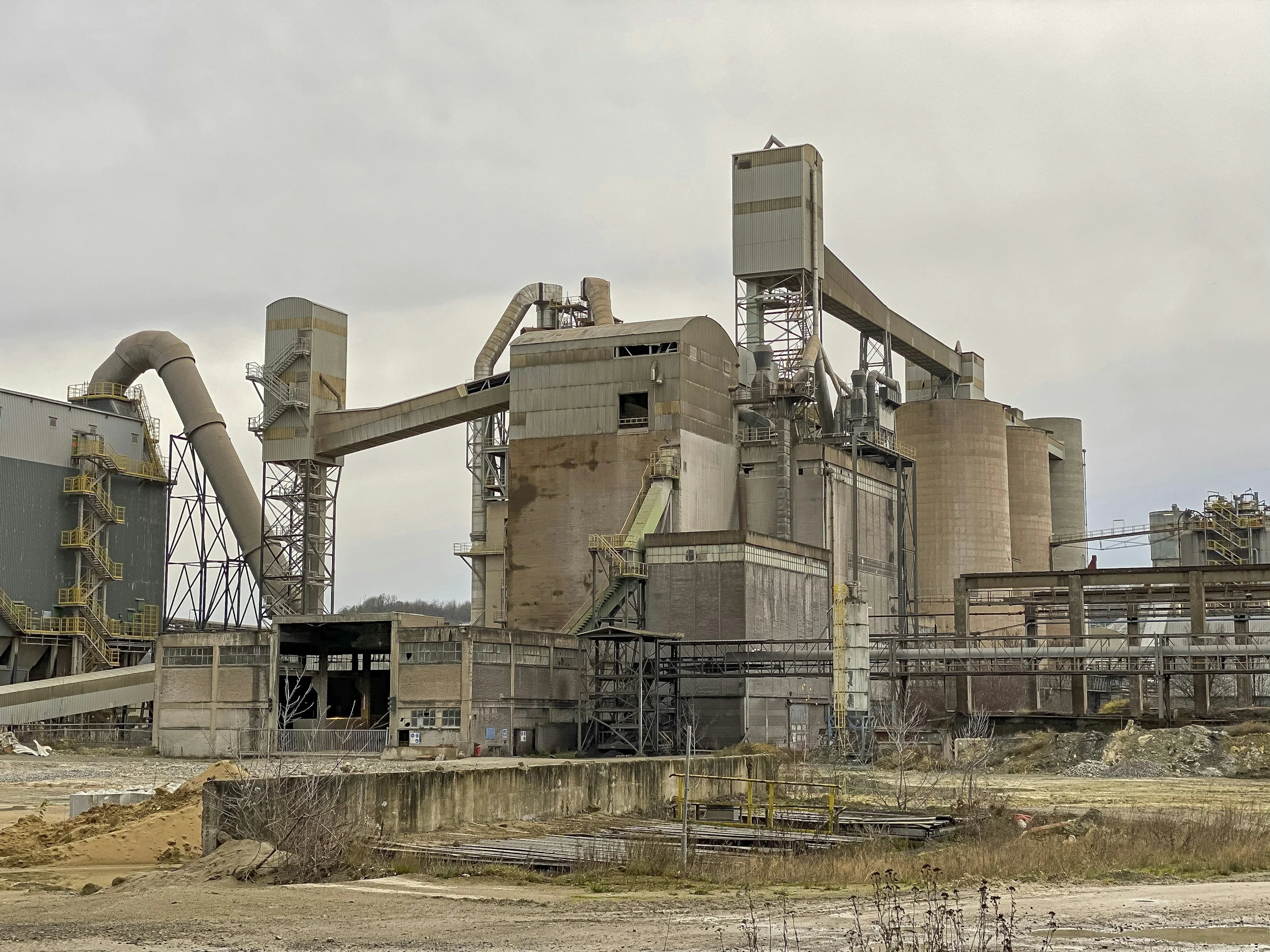 An industrial factory with large metal structures, pipes, and silos under a cloudy sky.