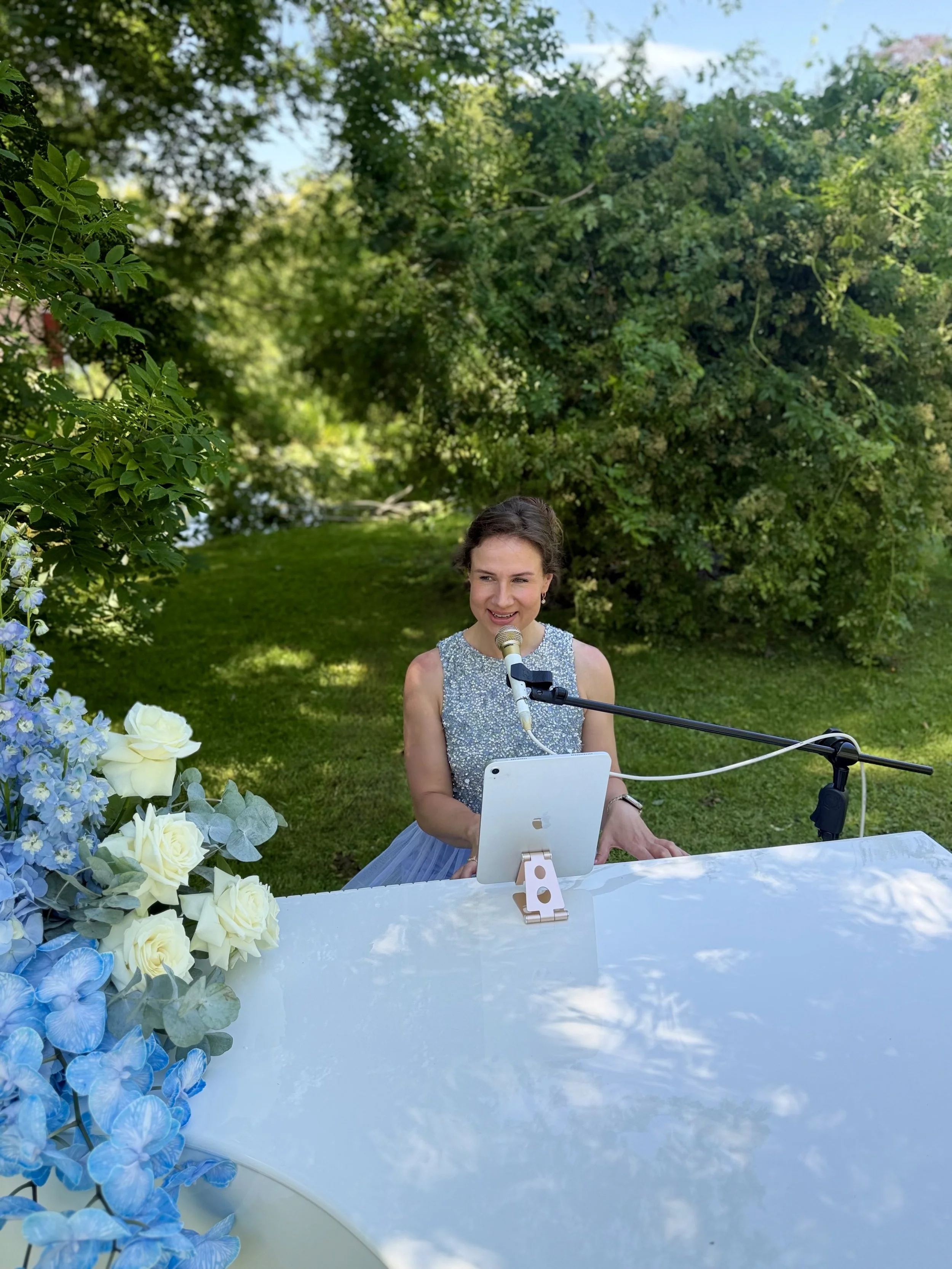 Kim Brooklyn singing and playing a white piano at an elegant outdoor event