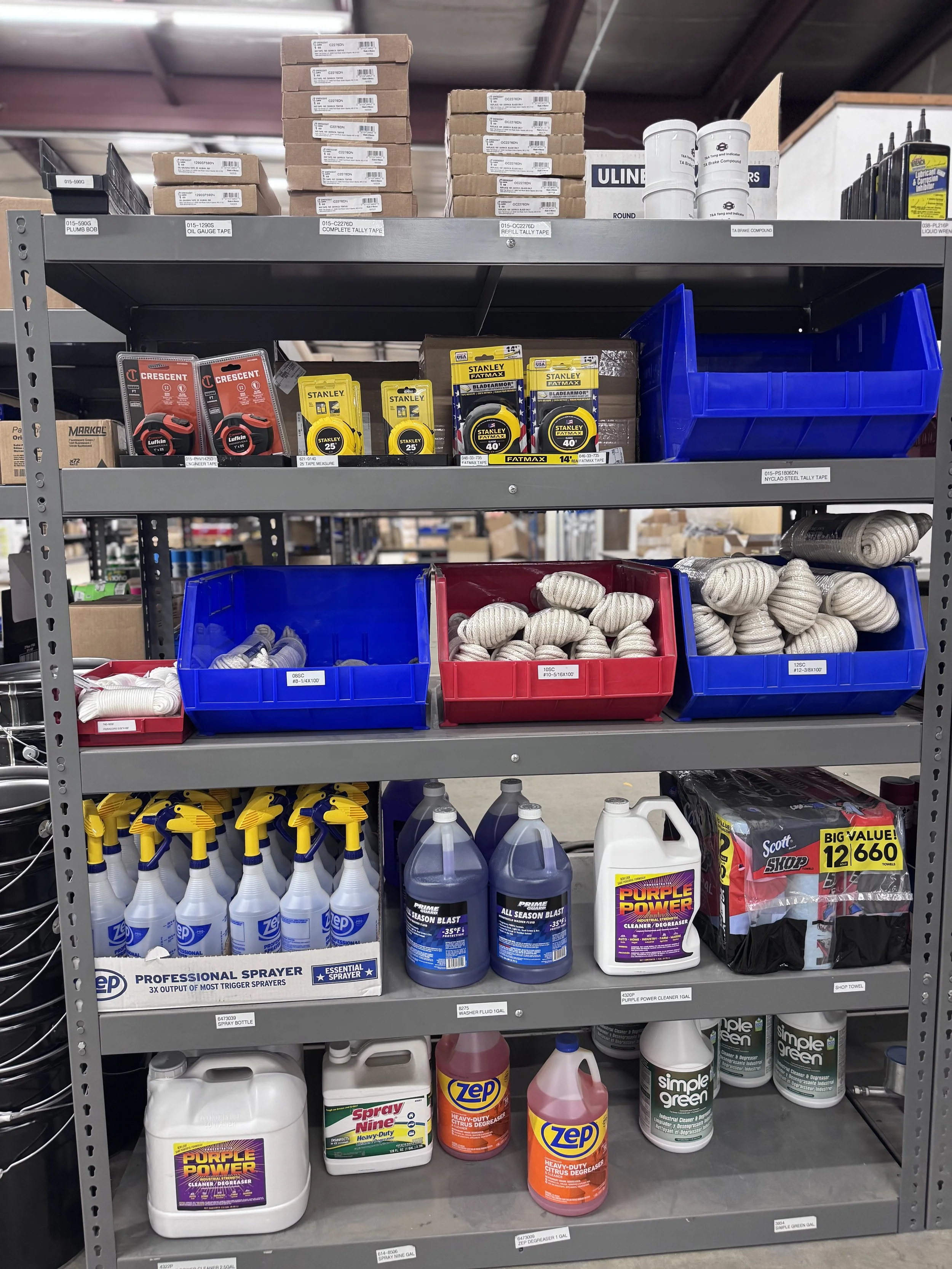 Shelving unit with various supplies including tape measures, rope, spray bottles, cleaning solutions, and storage boxes.
