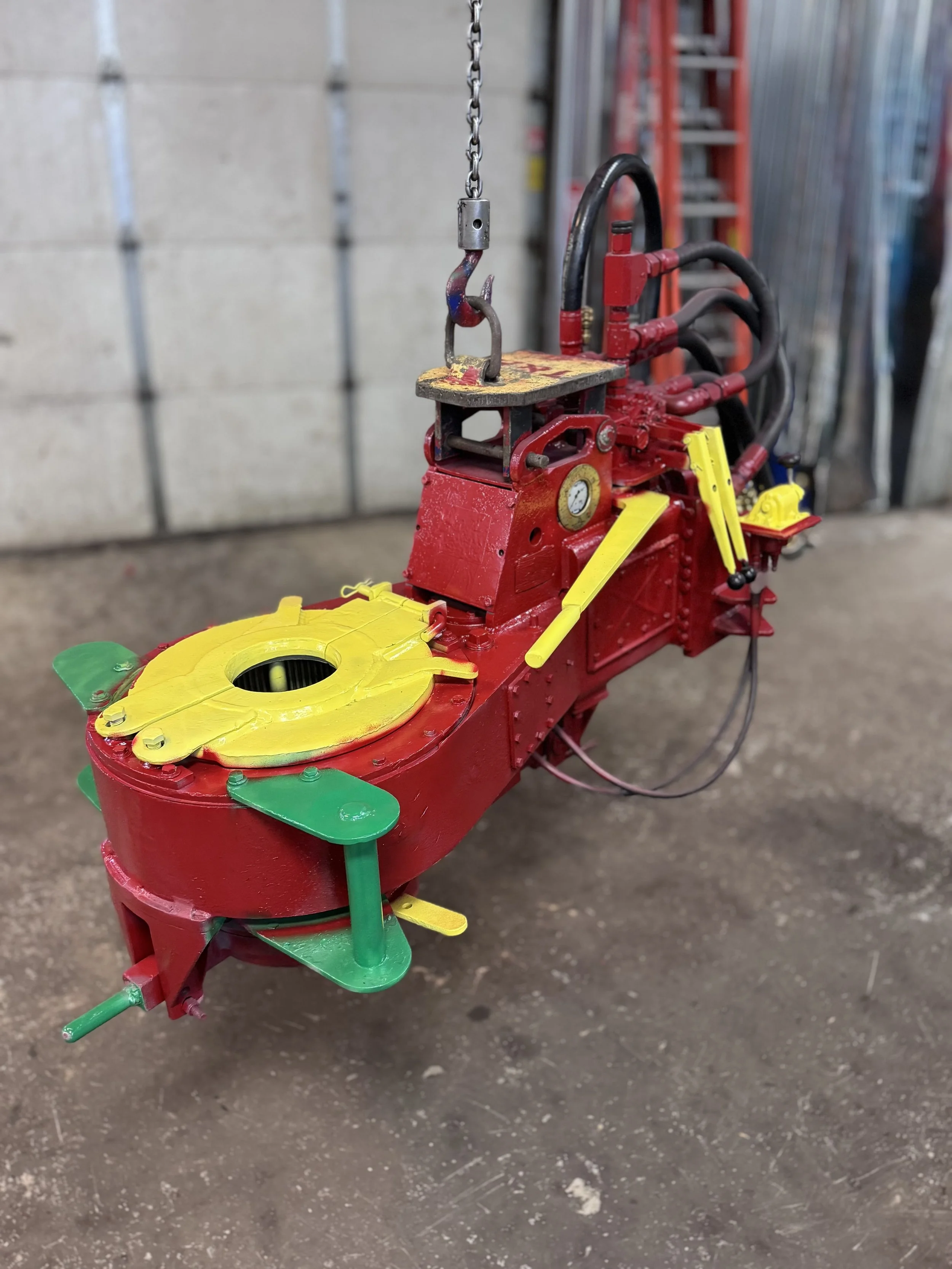A colorful, miniature cartoon-style model of a hydraulic excavator painted primarily red with yellow and green accents, placed on a concrete floor in an industrial setting.