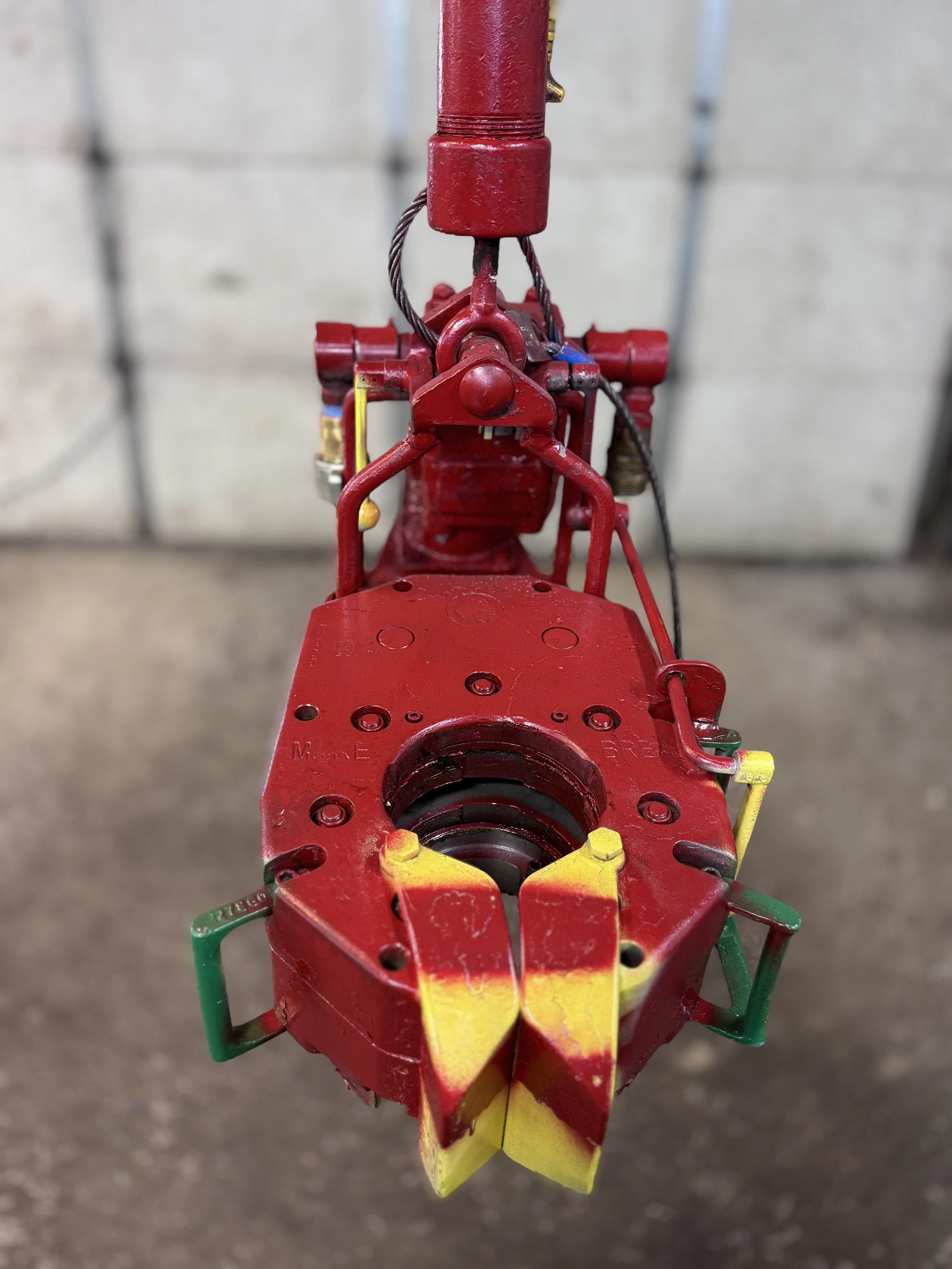 Close-up view of a red firefighter rescue tool with yellow and green markings, positioned on a rough concrete surface, with a background of gray garage doors.