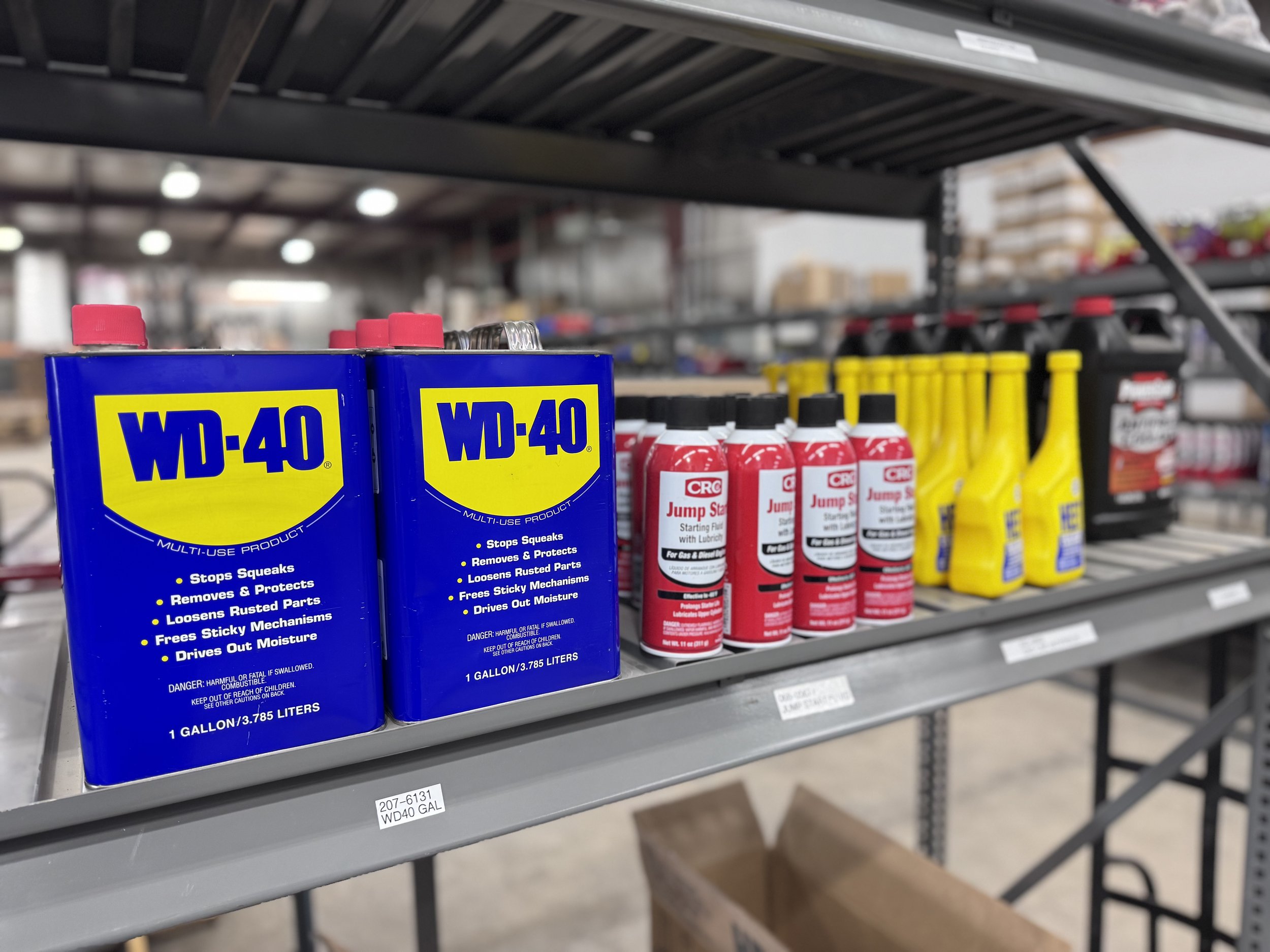 On store shelves, there are large blue cans of WD-40, red bottles of CRC Jump Start, and yellow bottles of Eazy Fuel.