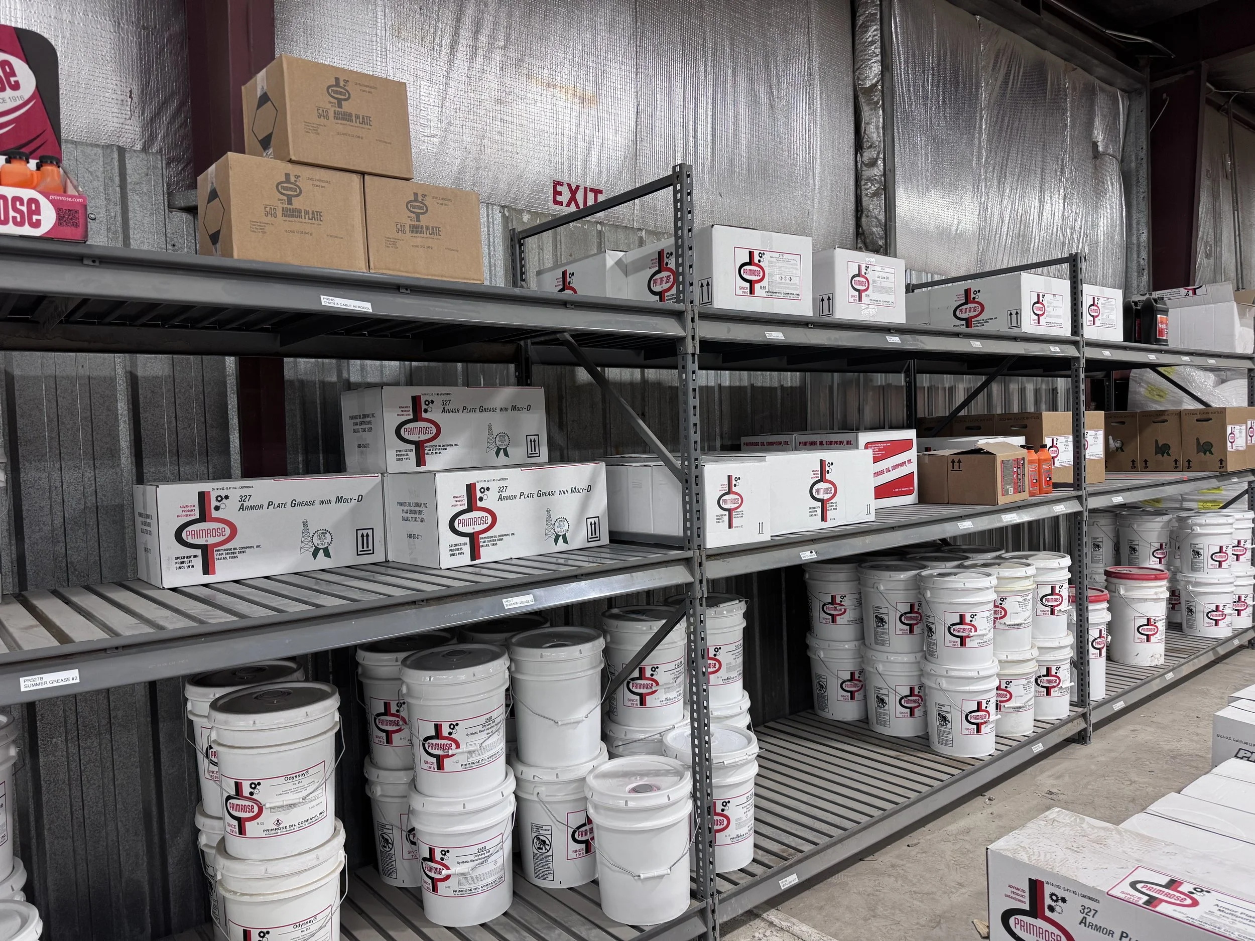 Industrial storage shelves filled with white buckets and boxes, labeled with Primrose branding, in a warehouse.