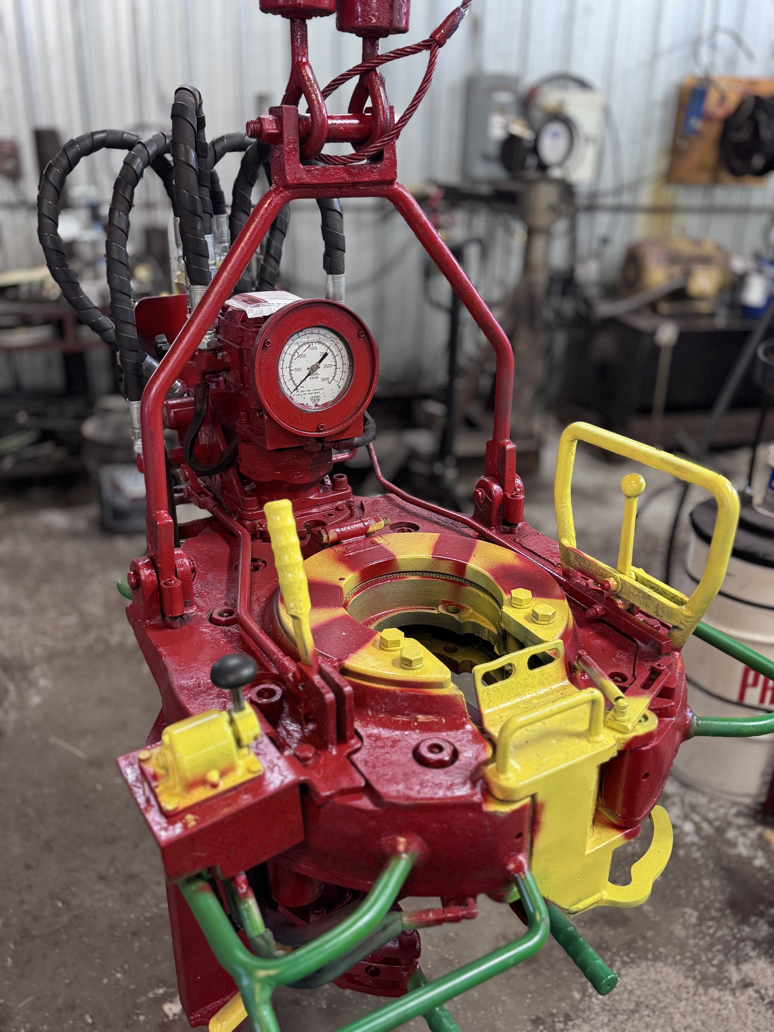 A red and yellow mechanical device with gauges, levers, and pipes, in a workshop setting.