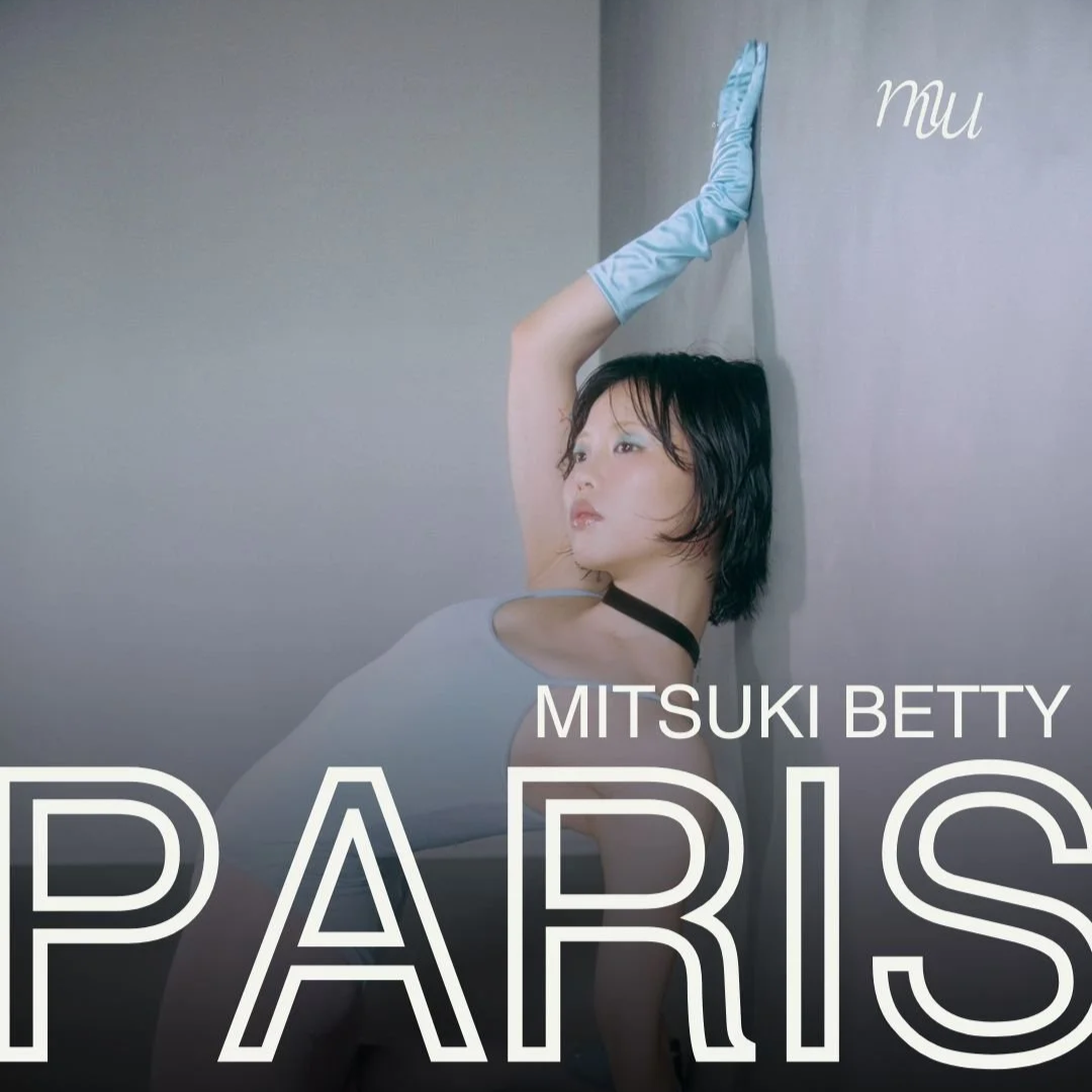 A woman with short dark hair wearing a sleeveless top and long satin gloves posing with one arm against a wall, with the text 'Mitsuki Betty Paris' on the image.