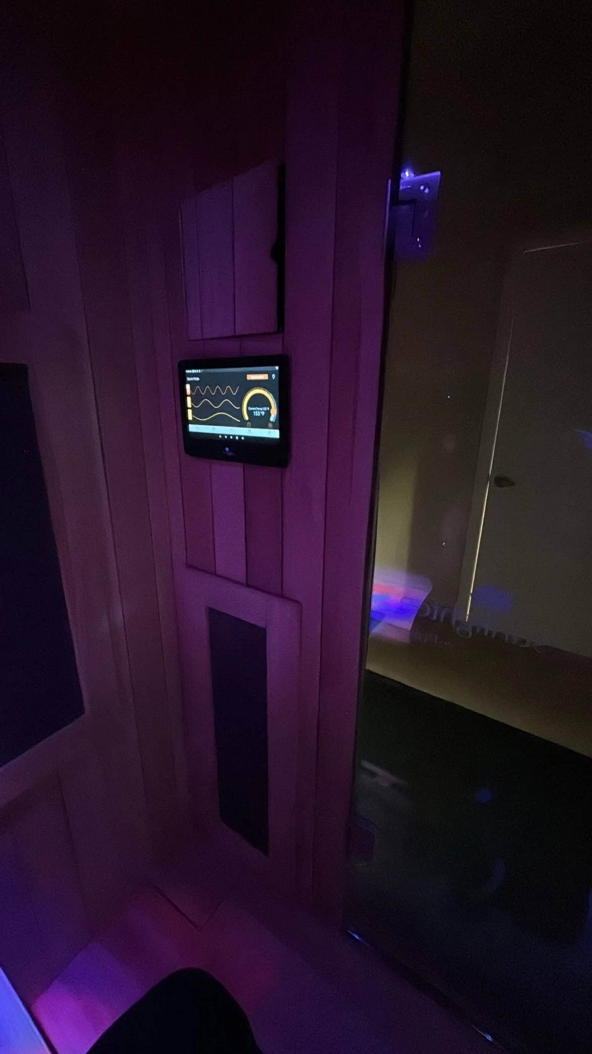 A wooden wall panel with a small screen displaying health or fitness data, next to a reflective glass door.