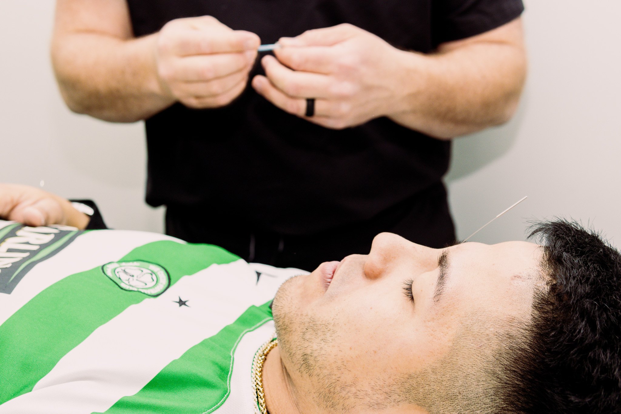 A man lying on an examination table, eyes closed, receiving an acupuncture treatment from a healthcare professional.