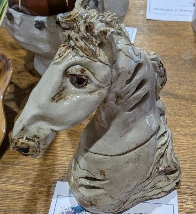Ceramic sculpture of a horse's head on a wooden table.