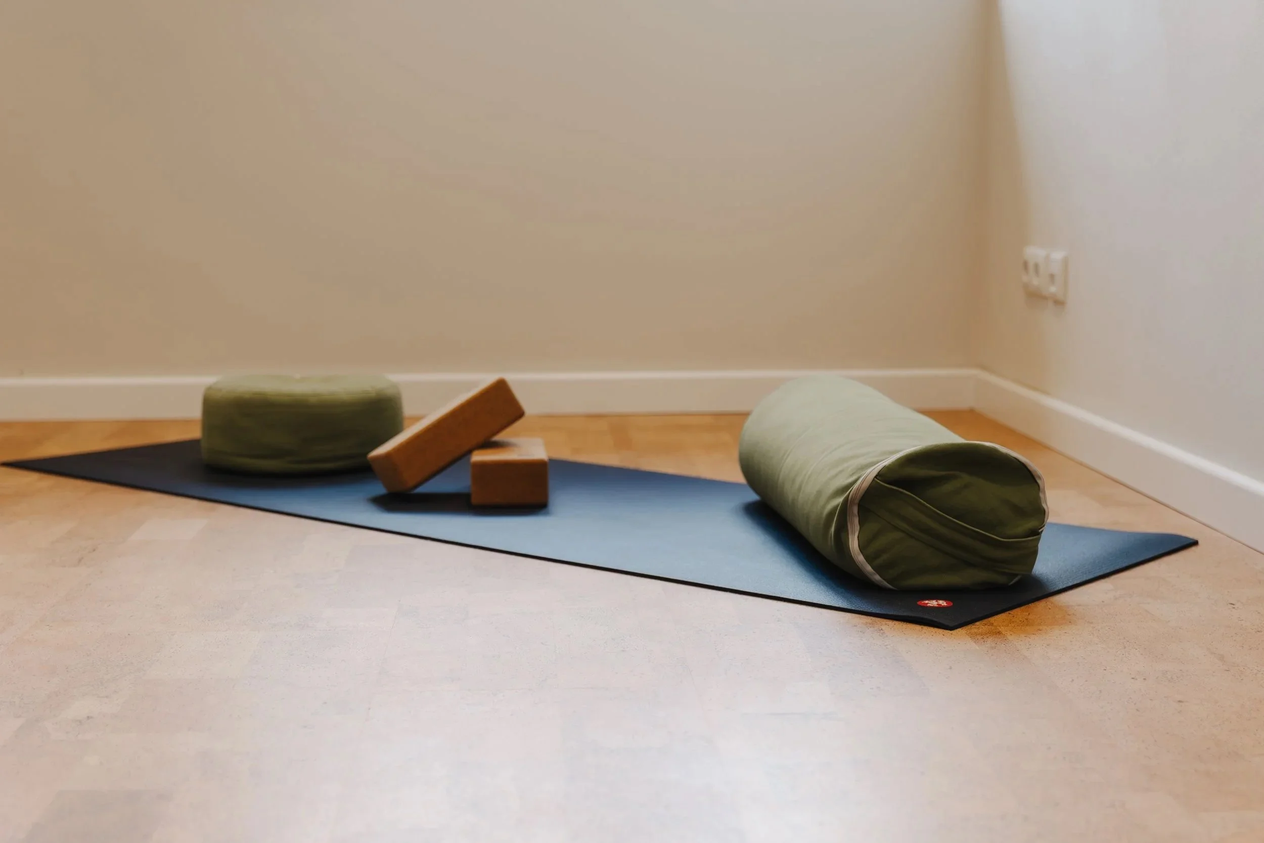 Yoga-Matte mit Yogablock, Bolster, Kissen und einem aufgerollten Yoga-Plan