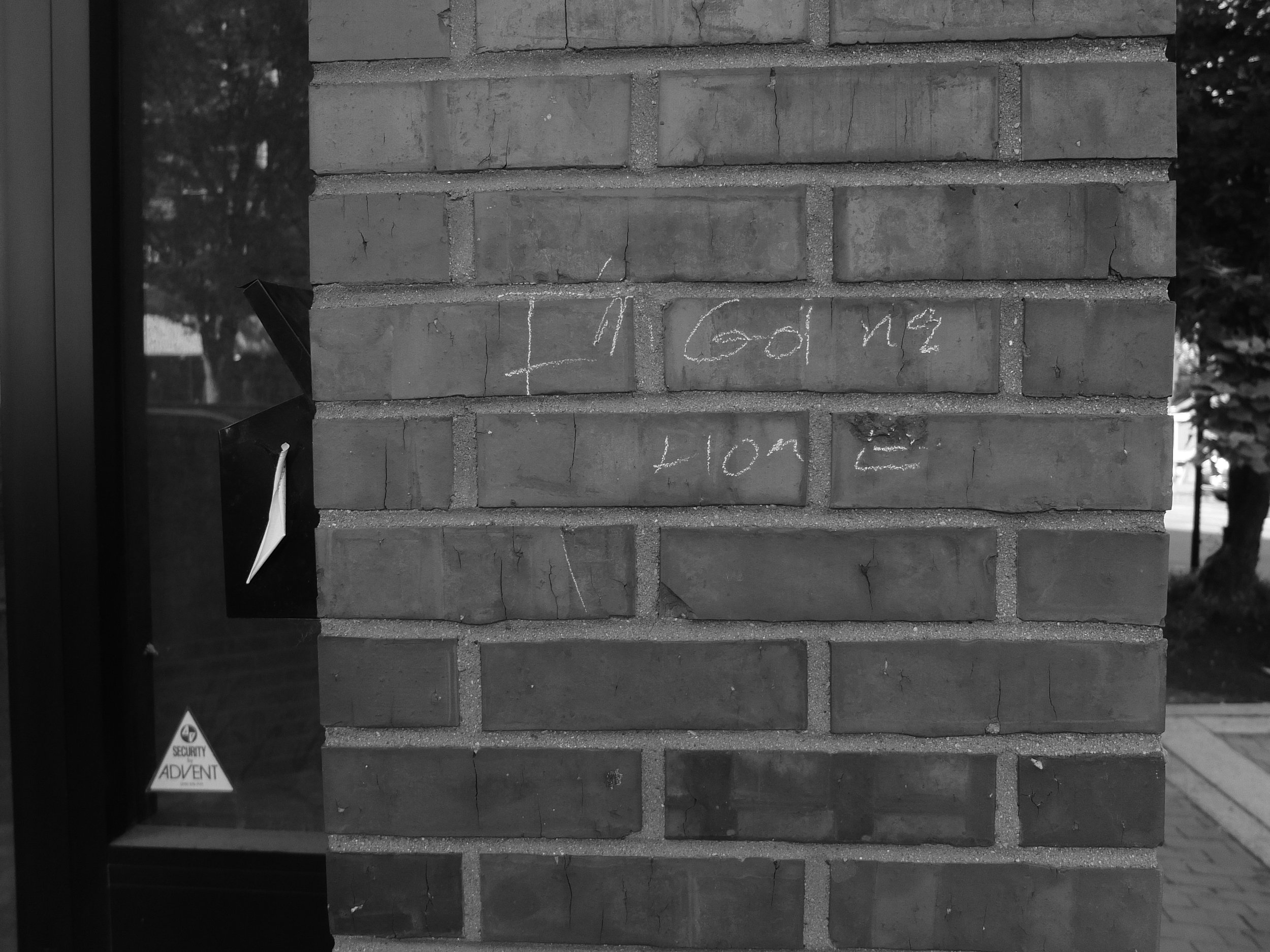 Black and white photo of a brick wall with chalk writing that reads "I'm going home". There is a window frame on the left side.