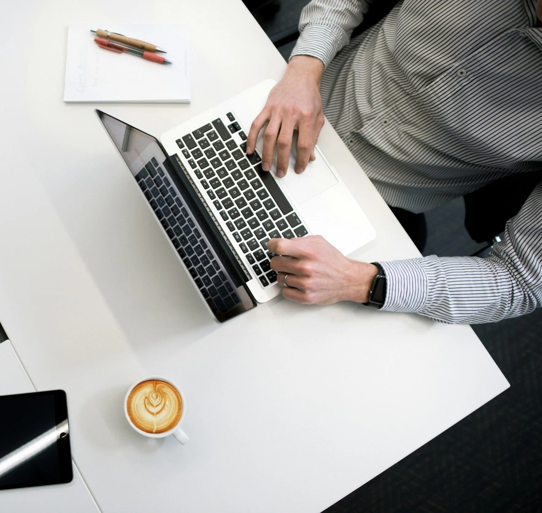 A person working on a laptop at a white desk with a coffee cup and a smartphone.