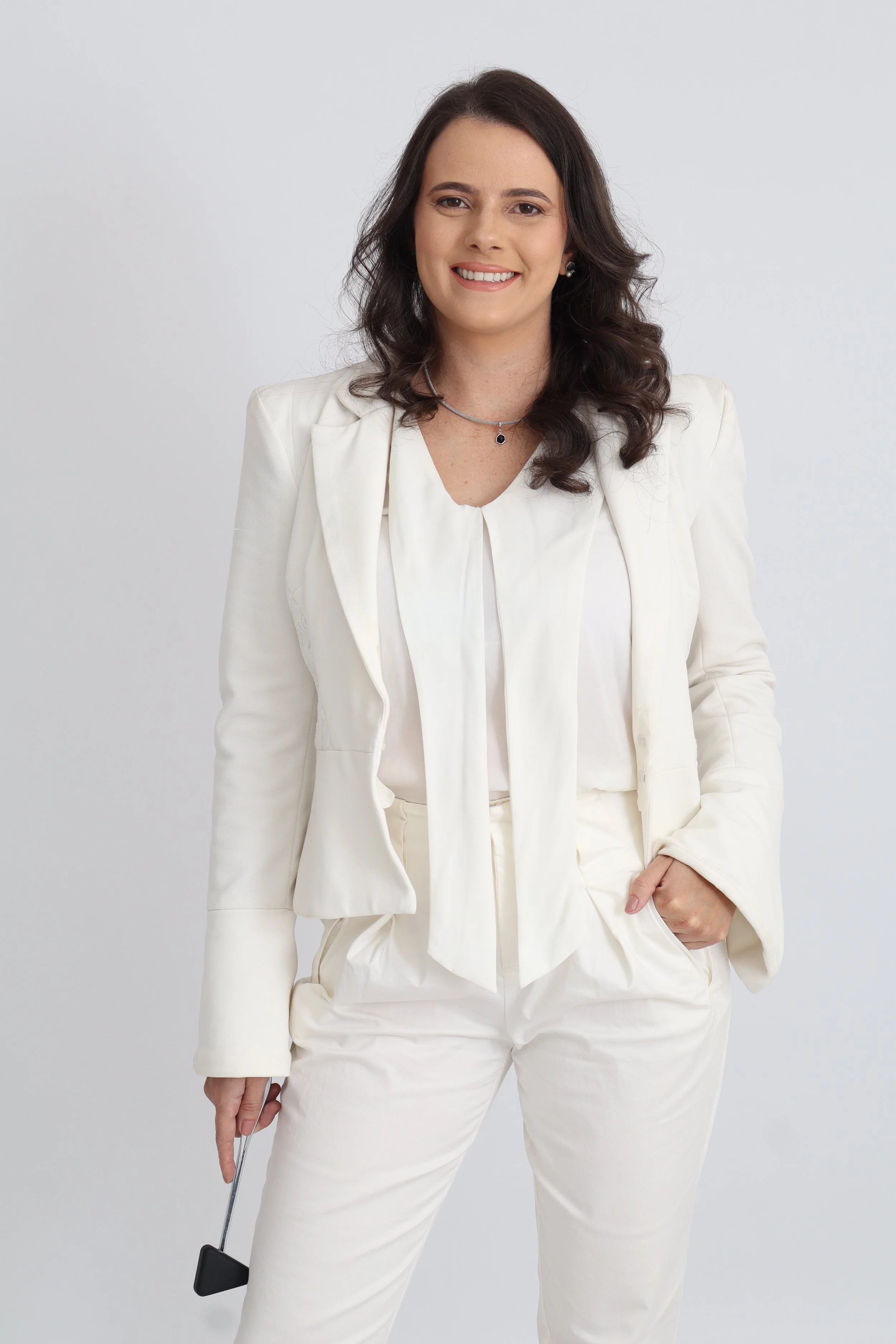 Mulher vestida de branco, sorrindo, com cabelo castanho ondulado, segurando um taco de golfe, em um fundo cinza claro.