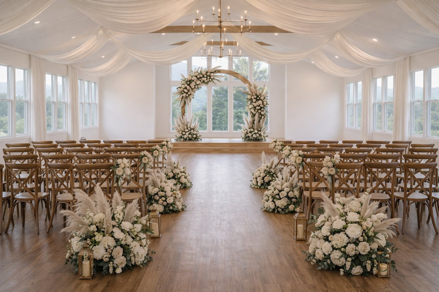 Empty wedding ceremony space with wooden chairs, floral arrangements, a circular floral arch, and a white draped ceiling with chandeliers.