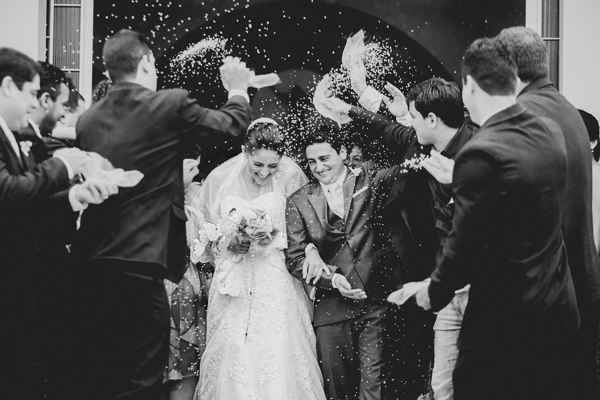 A bride and groom walking through a crowd of people celebrating with confetti at their wedding.