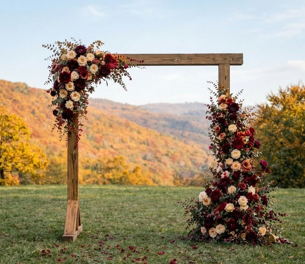 Wooden wedding arch decorated with a large floral arrangement of red, pink, and white flowers, set outdoors with mountains and trees in the background.