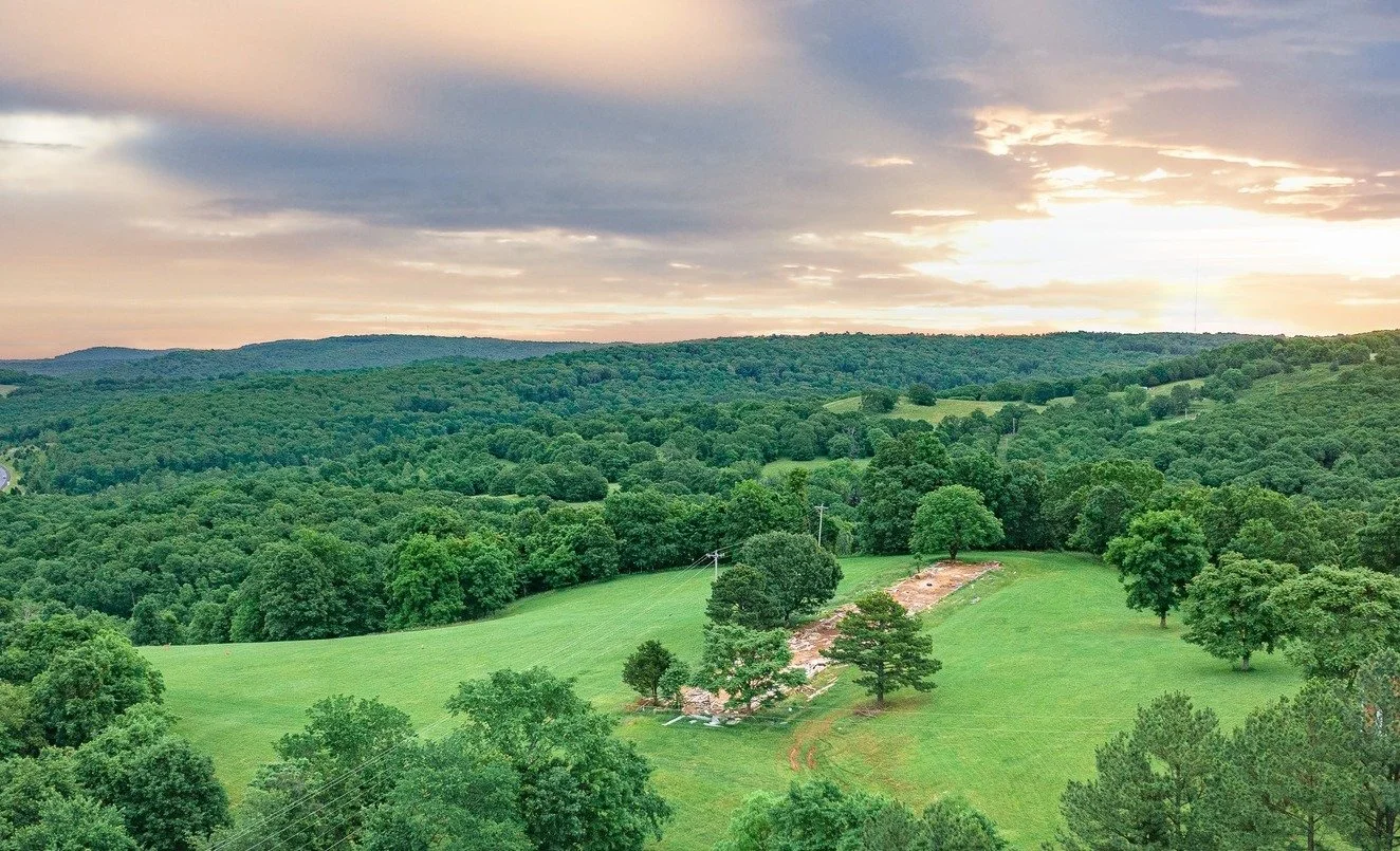Scenic view of green rolling hills and dense forest with a partly cloudy sky at sunset