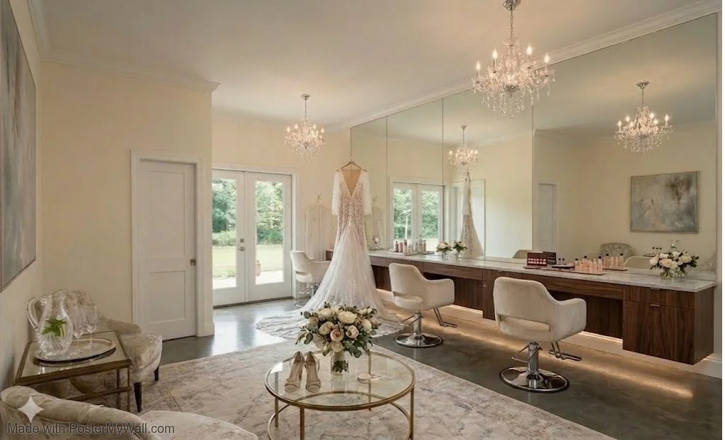 A bridal dressing room with a wedding dress, chairs, mirror, chandelier, and floral arrangements.
