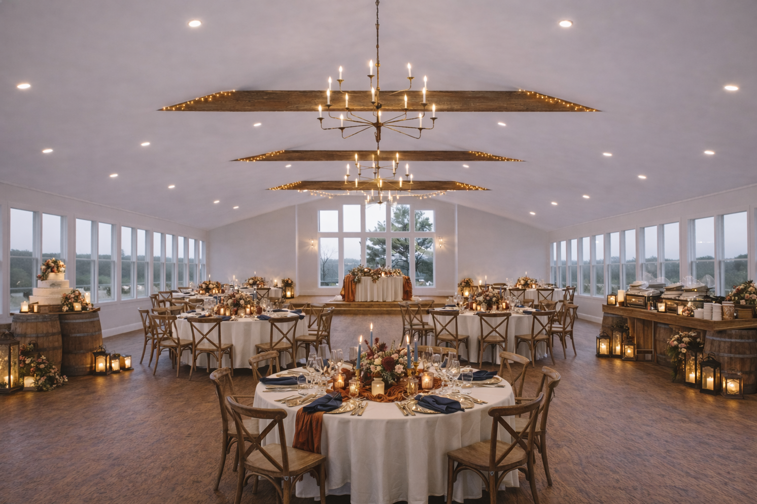 Elegant wedding reception in a large, bright room with wooden floors, featuring round tables with white tablecloths, floral centerpieces, candles, and navy blue napkins. The room has large windows on both sides, a high ceiling with wooden beams, and 