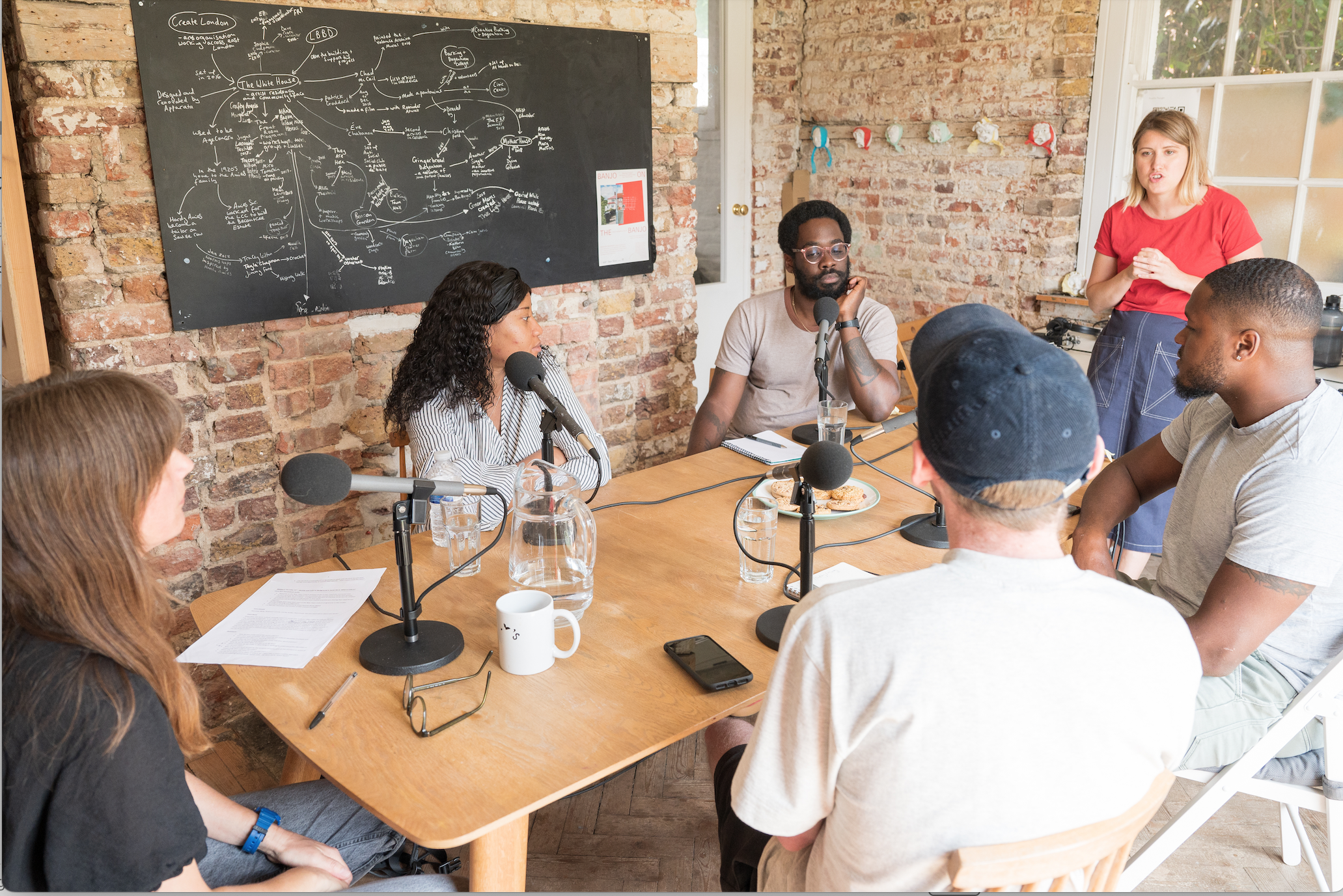 6 adults sitting around a table with microphones to record a podcast