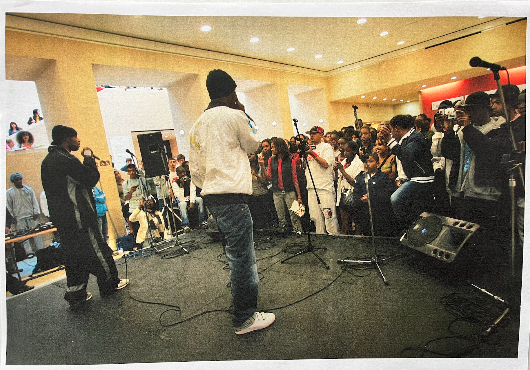 Image taken from behind two young men performing vocals with mics in front of a large audience of young people in Tate Britain.