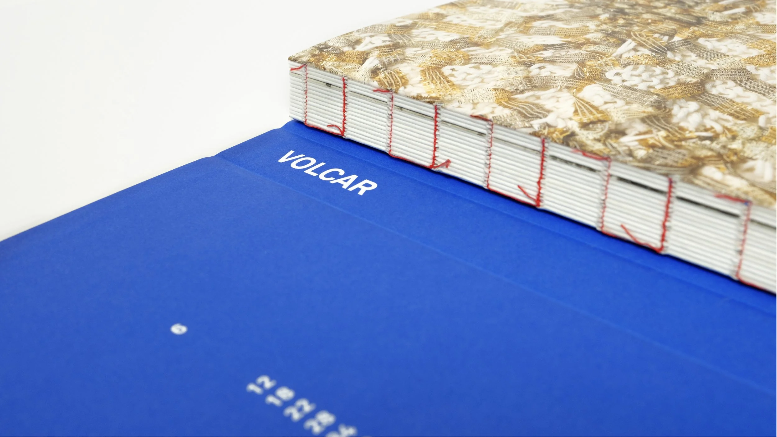 Libro con copertina rigida blu con la scritta 'VOLCAR'. Si vede la rilegatura svizzera con cucitura a filo refe in cotone color rosso.