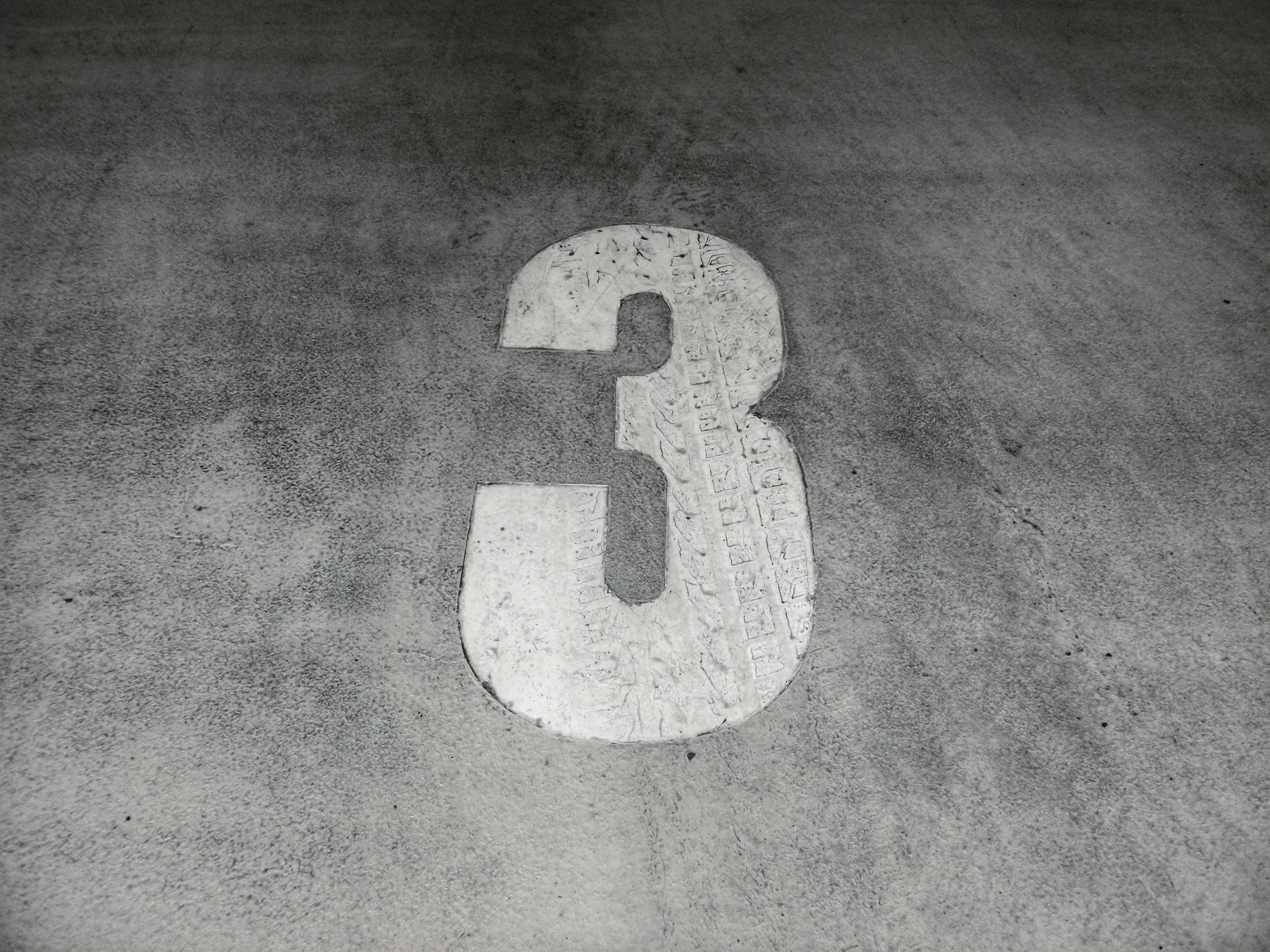 A white painted number 3 on a textured concrete surface.