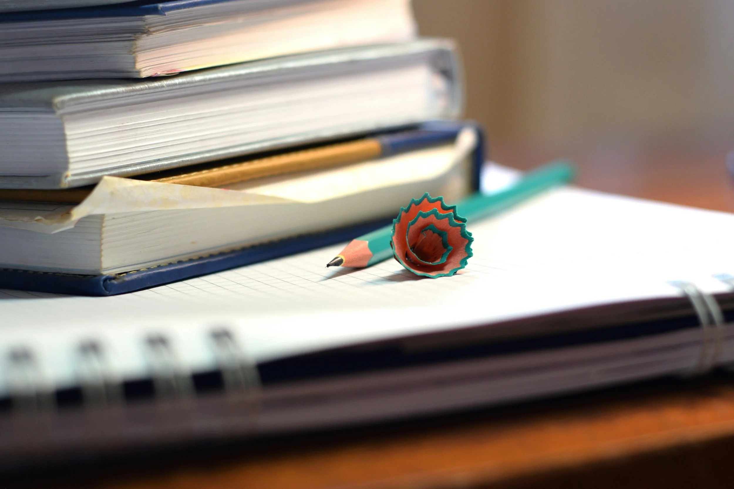 Stack of books, a spiral notebook, a pencil, and a pencil eraser on a desk.