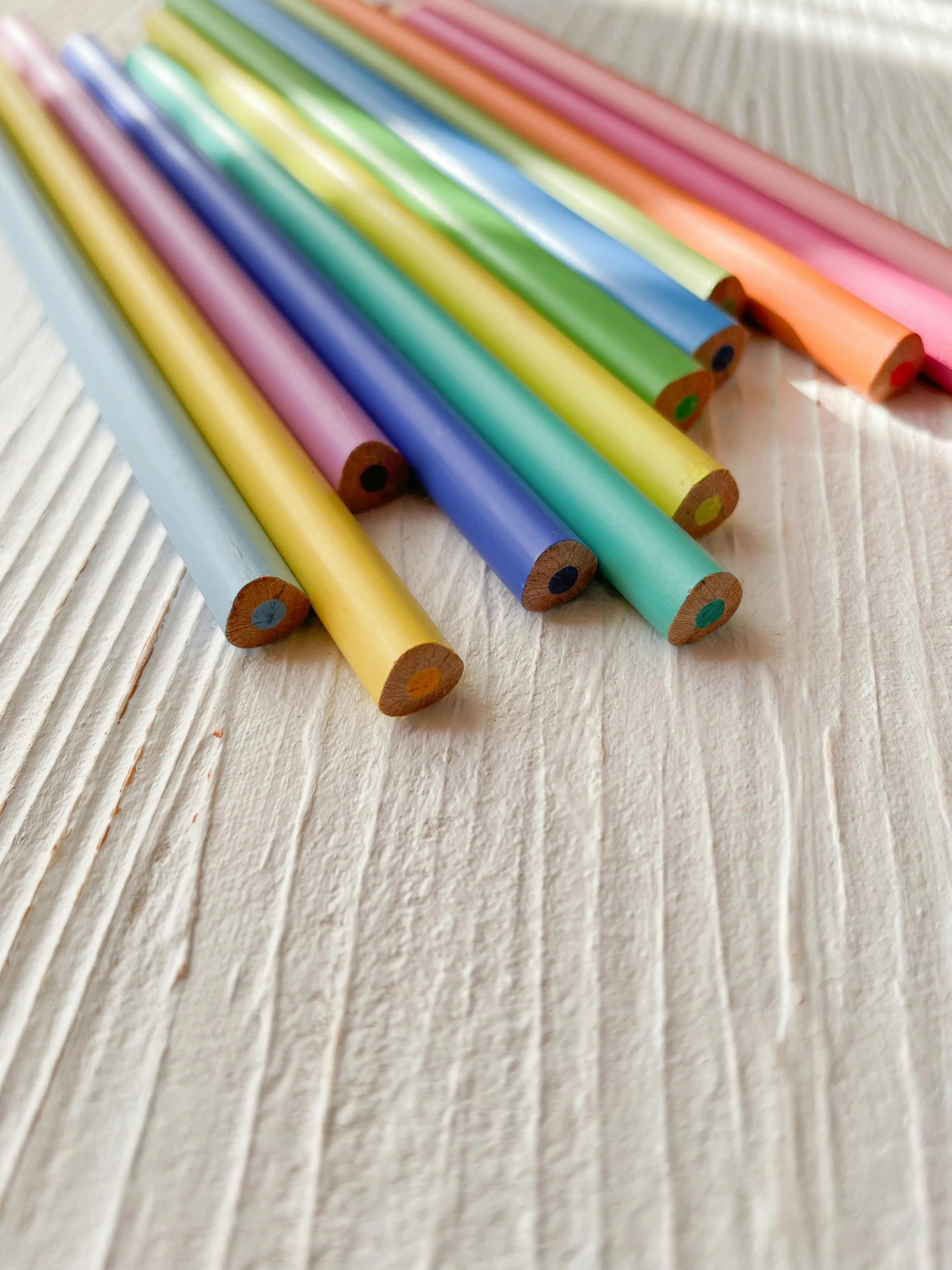Colorful wooden pencils arranged on a white textured surface.