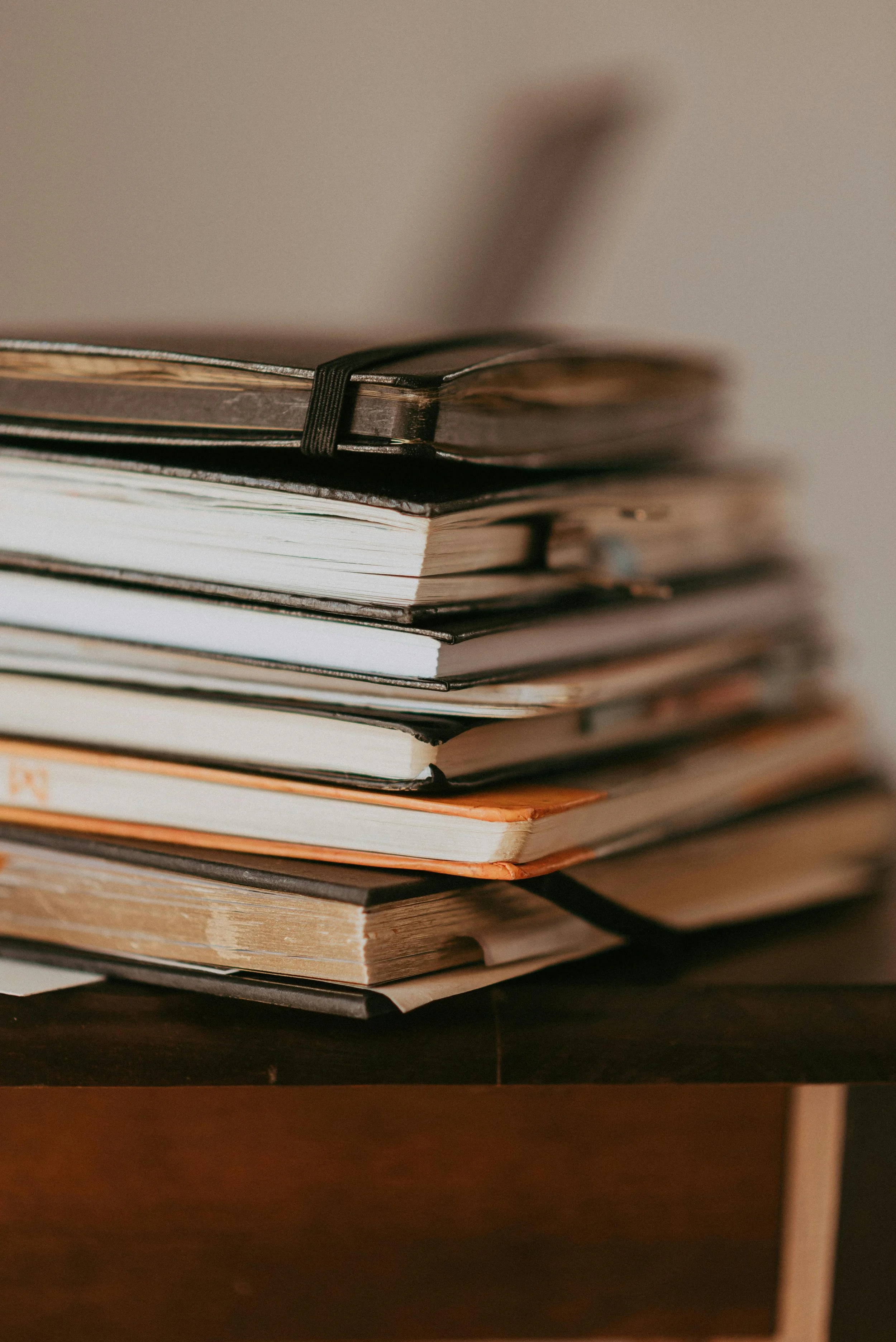 A stack of various magazines and notebooks on a dark wooden surface.
