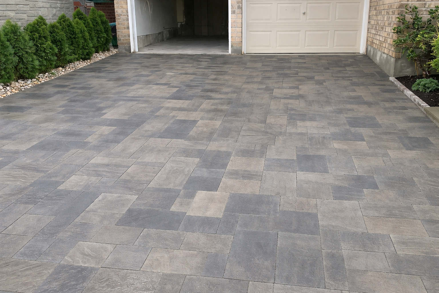 A concrete driveway leading to a garage door, bordered by green shrubs on the left and a flower bed with plants on the right.