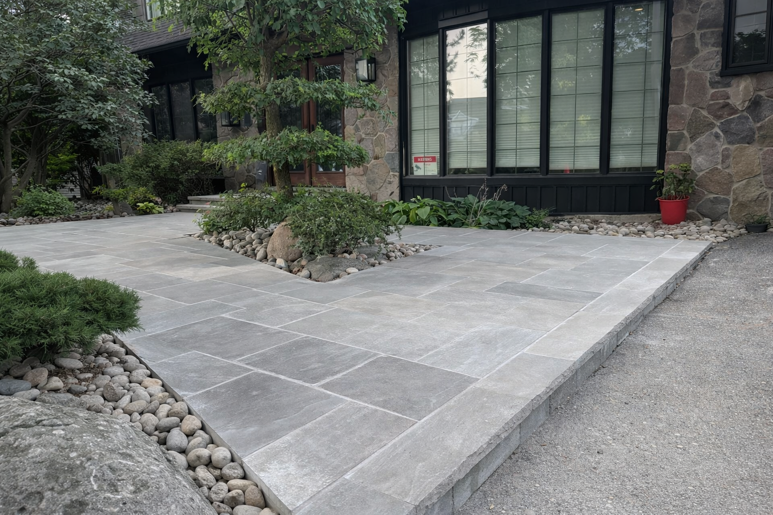 Modern house with stone facade, large front window, and a landscaped stone path with plants and small trees