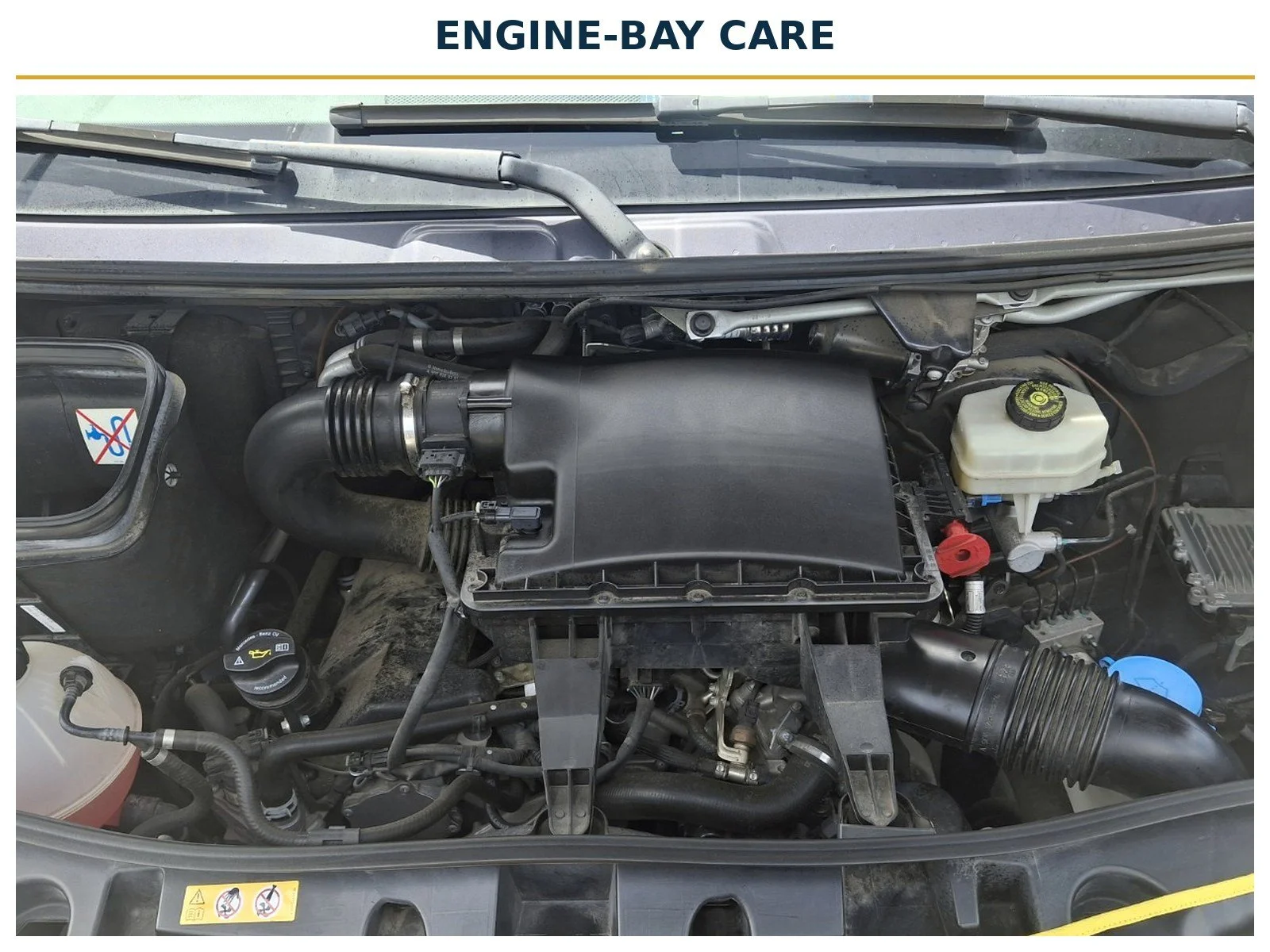 Mercedes-Benz Sprinter engine bay with the air-filter housing, fluid reservoirs and a protective cover across the front of the vehicle.