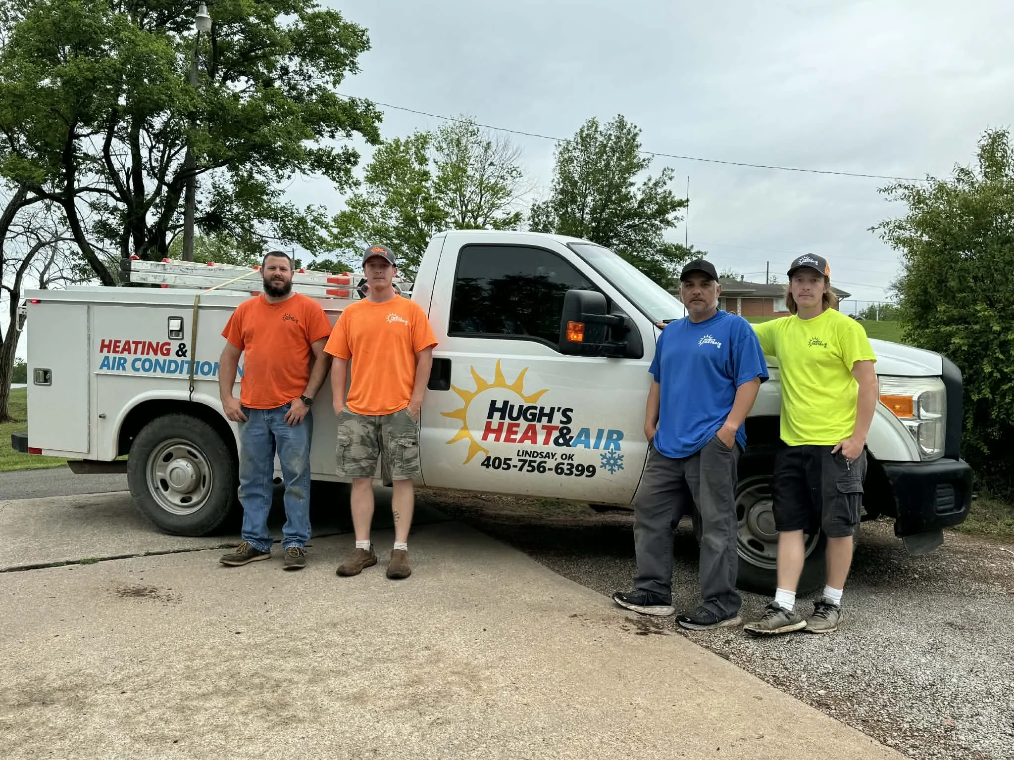 Four men in colorful shirts standing around a work truck featuring a logo with Heat & Air and a sun. 
