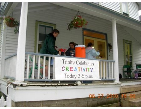 People on a porch celebrating Trinity's creativity event with a table, supplies, and a banner.